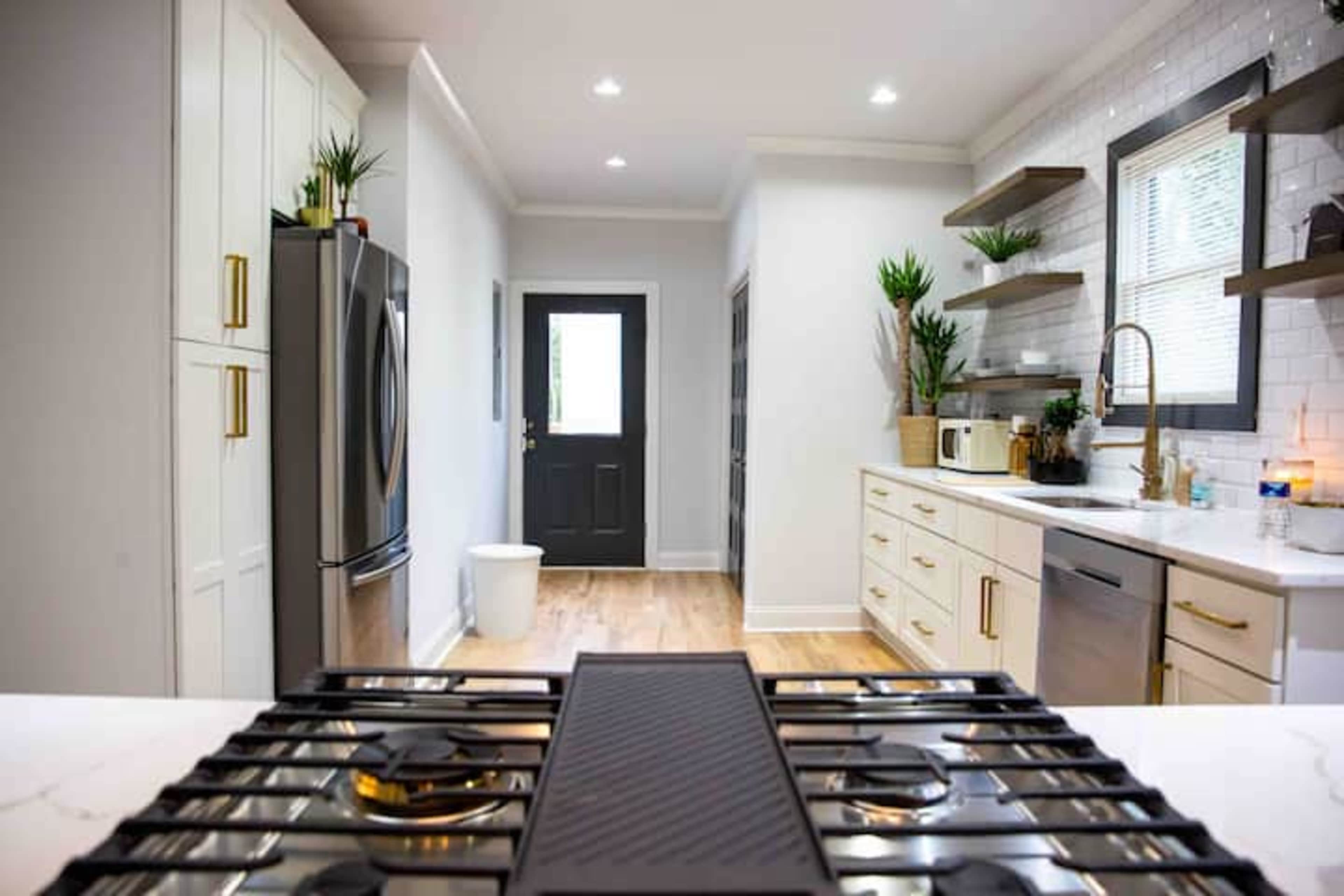A modern kitchen with a gas stove in the foreground, sleek cabinetry, and natural light coming through a door at the end of the room.