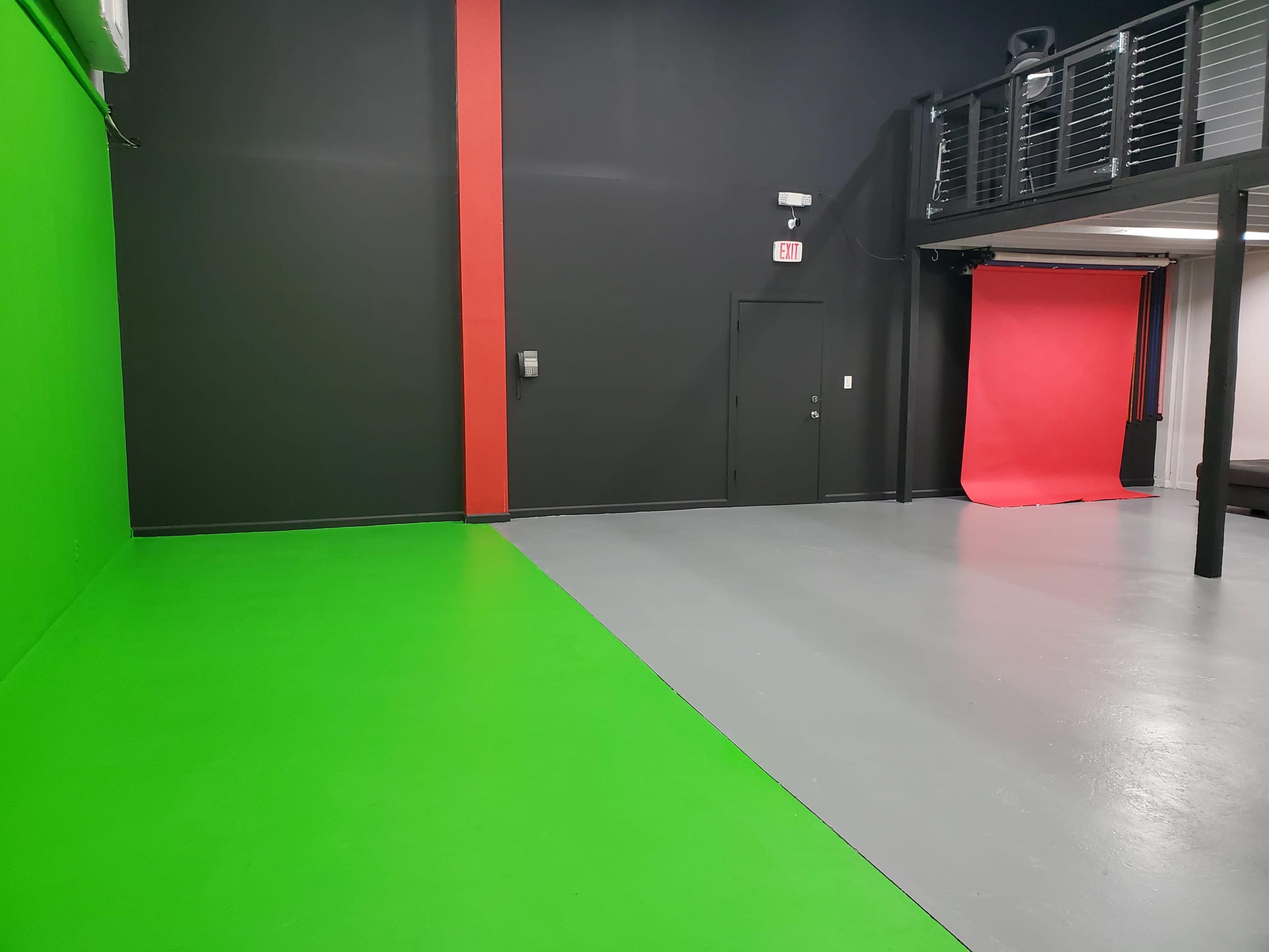 A studio space with a green wall on one side, a gray floor, and a red backdrop at the far end.