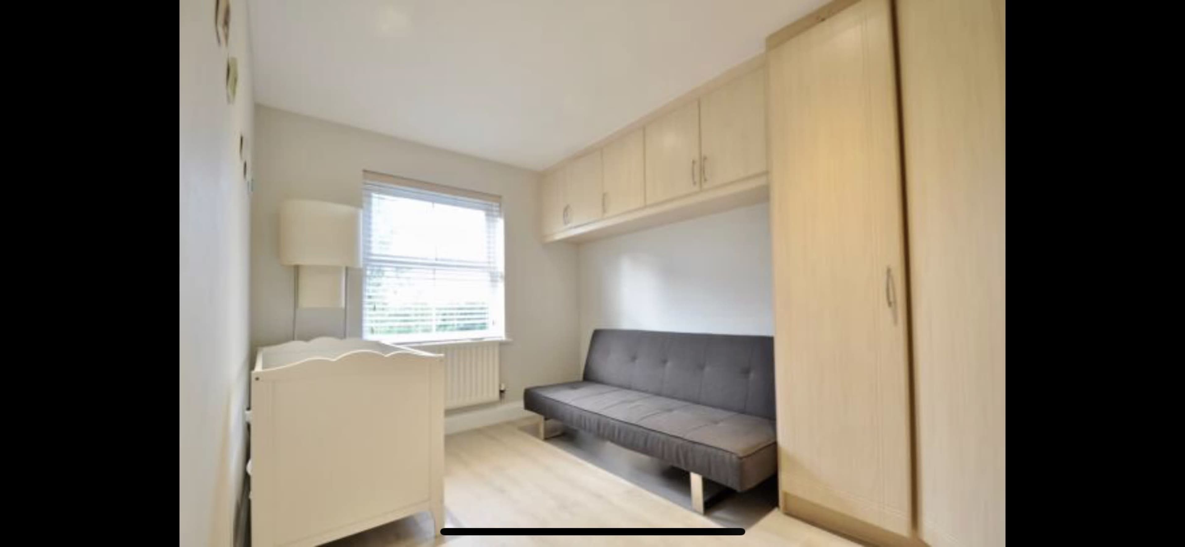 A small room with a light-colored wall, a gray sofa bed, a white dresser, and a window with blinds.