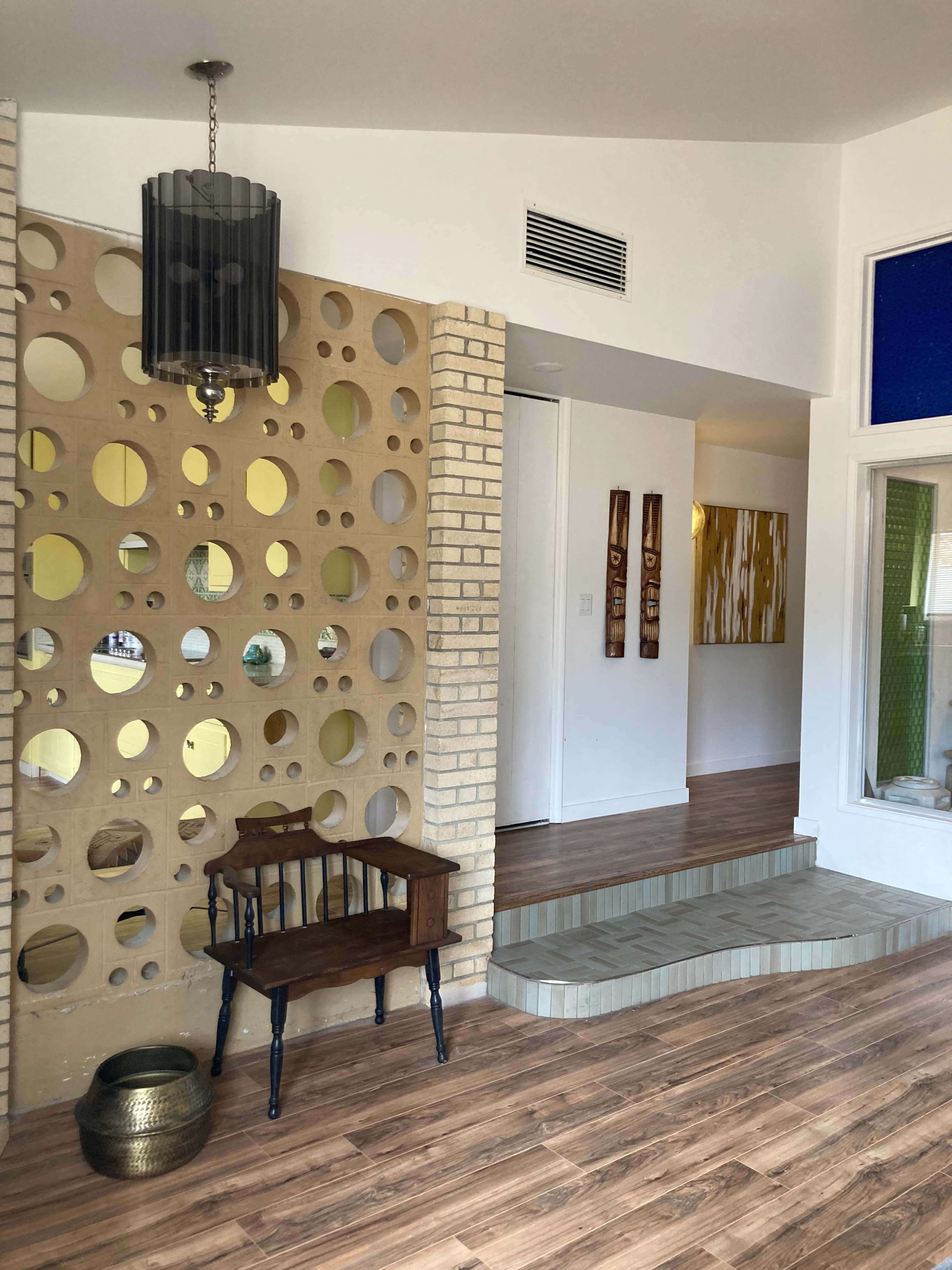 The image shows a modern entrance hall featuring a patterned wall, wooden flooring, and a small wooden bench with a decorative bowl.