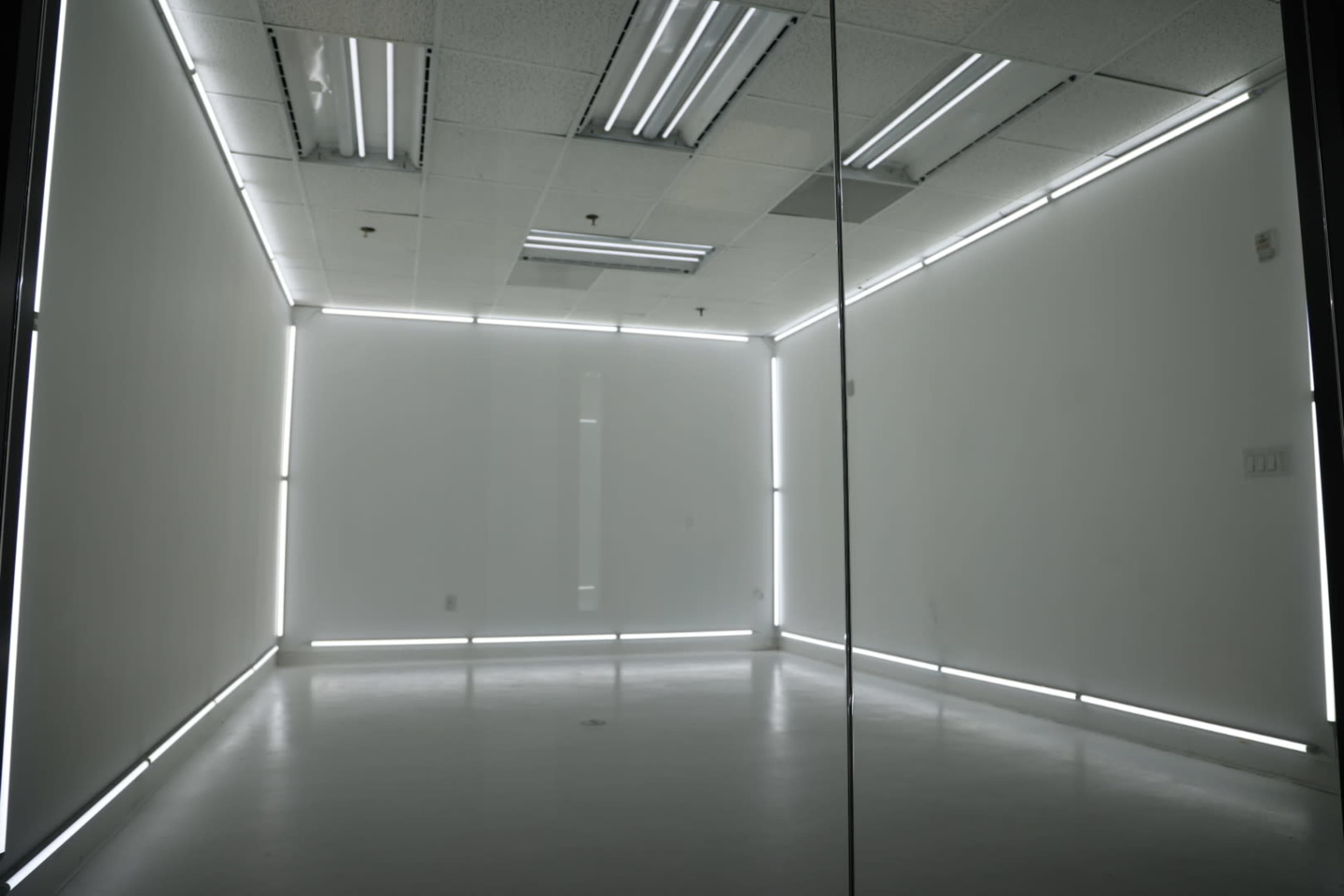A sparsely furnished, brightly lit room with white walls and edge lighting along the floor and ceiling.