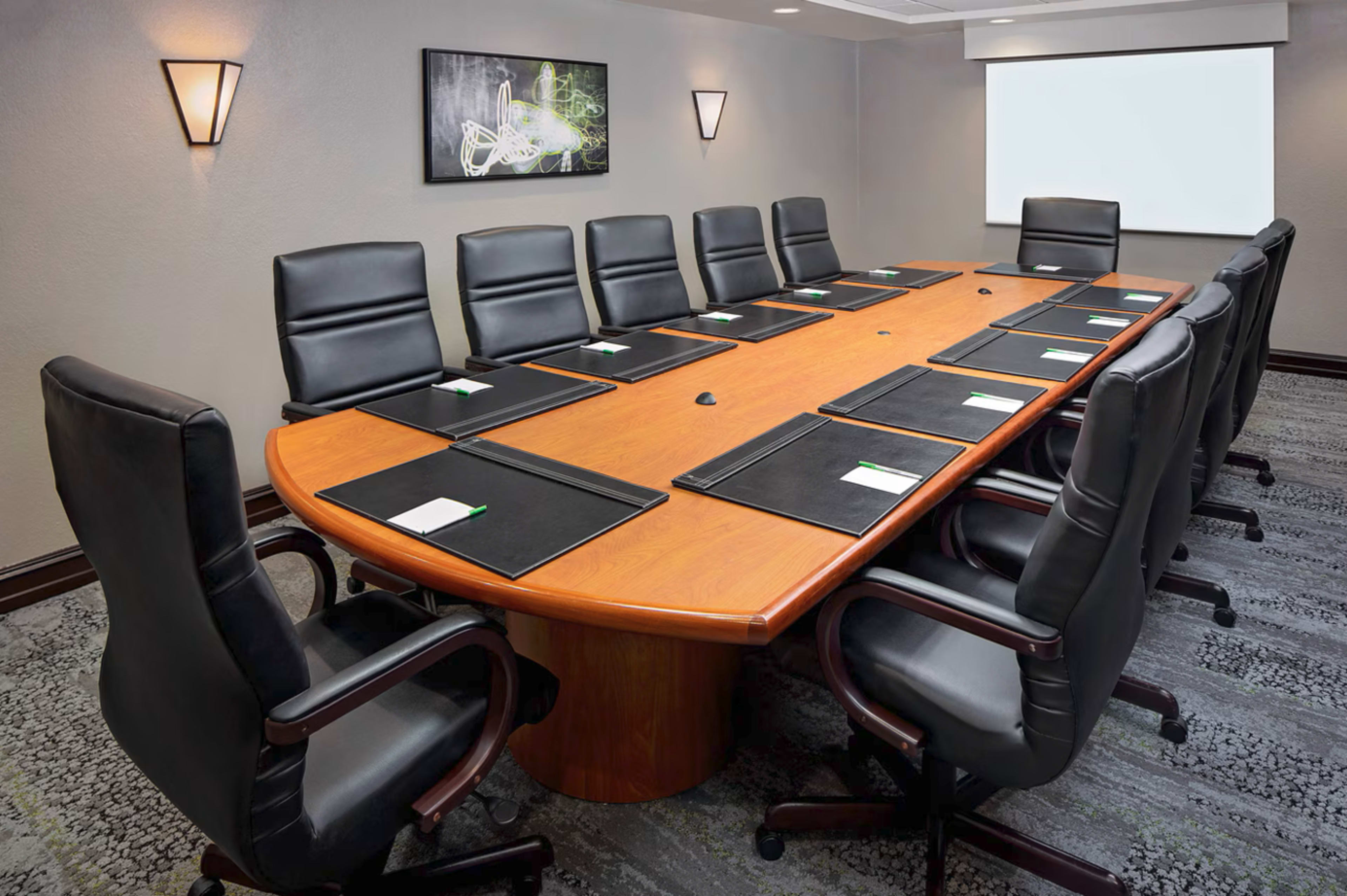 The image shows a large, oval conference table surrounded by ten black leather chairs in a well-lit meeting room.