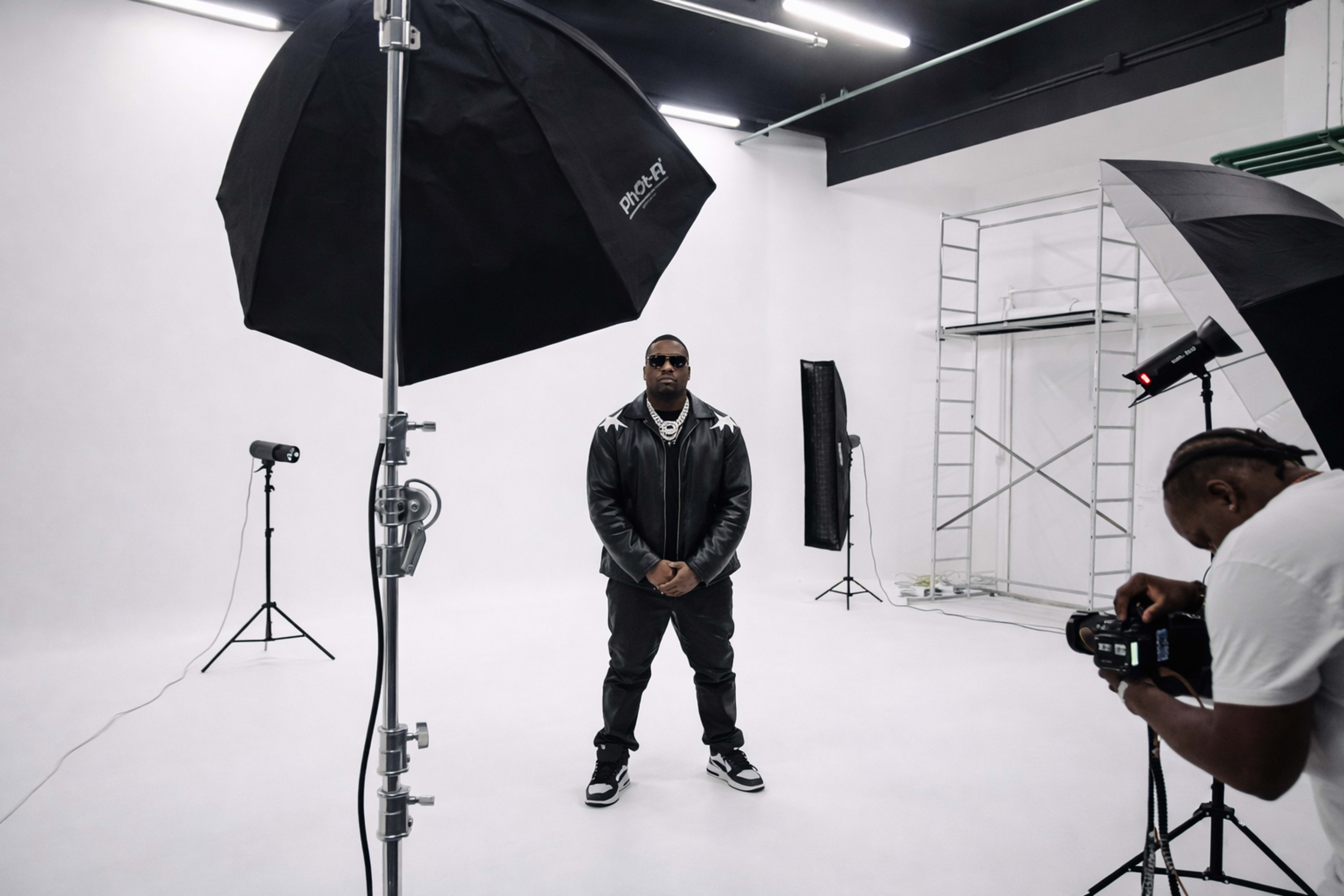 A person stands in a photo studio surrounded by lighting equipment and a backdrop.