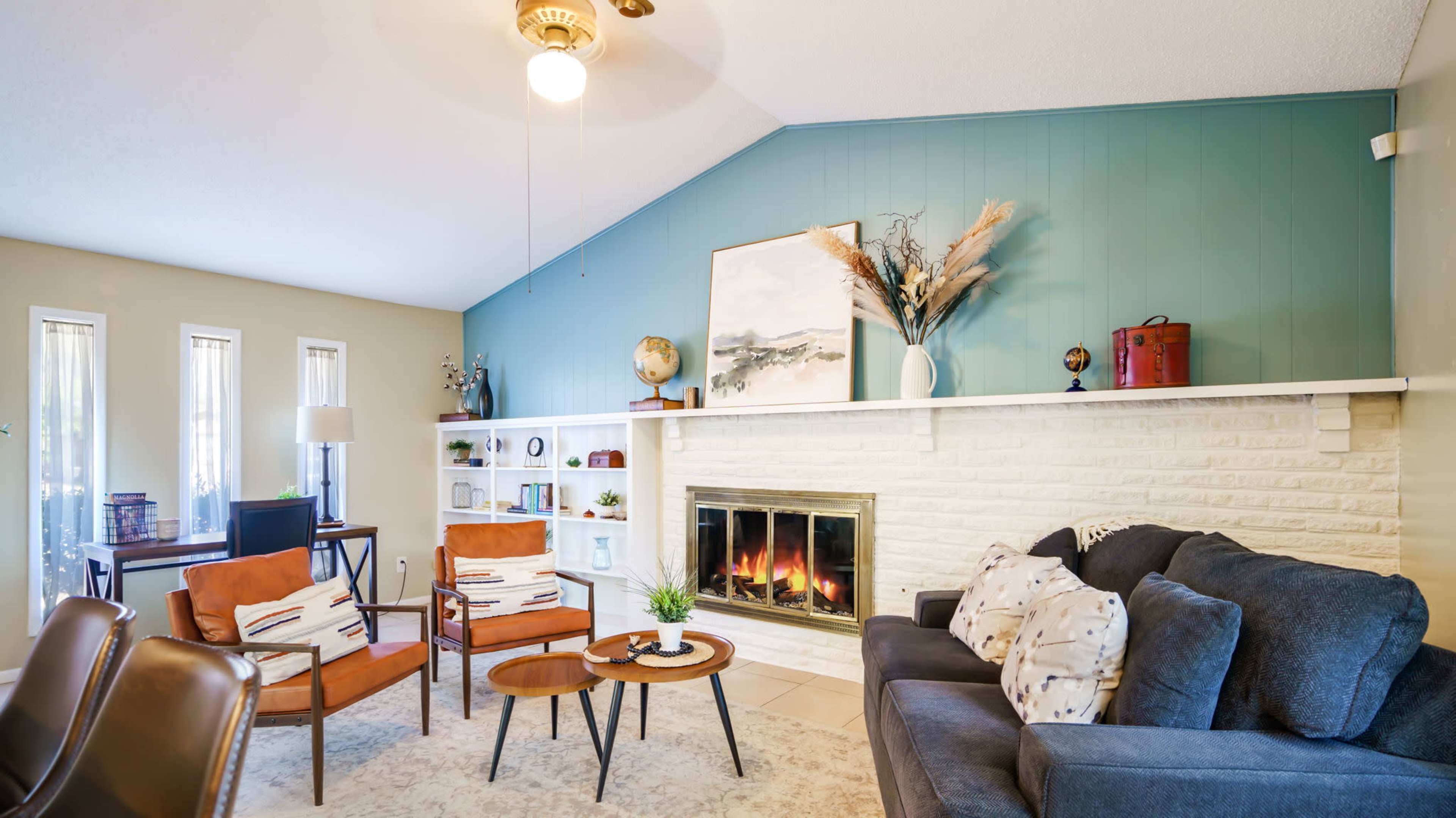 The living room features a fireplace with a white brick surround, two brown armchairs, a gray sofa, and shelves with decorative items.