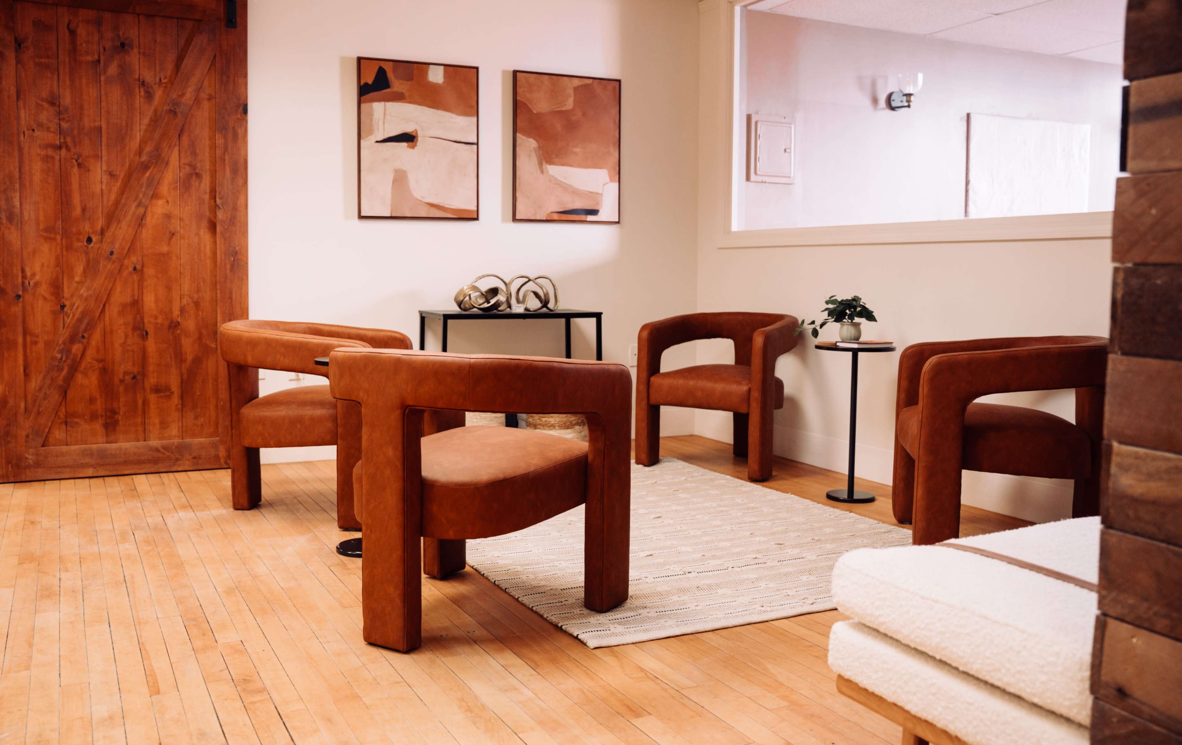 The image shows a cozy interior space featuring four brown upholstered chairs arranged around a small table on a light-colored rug.