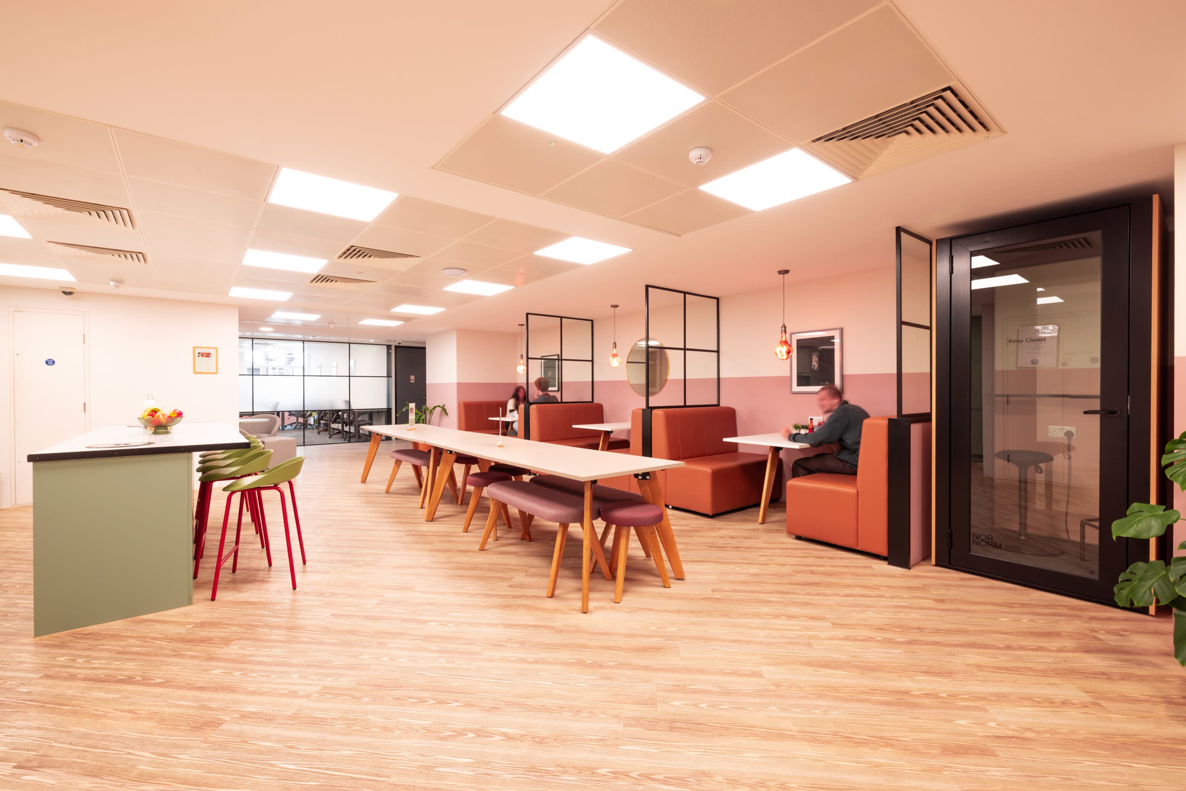 The image shows a modern office break room with tables, seating areas, and minimalist decor.