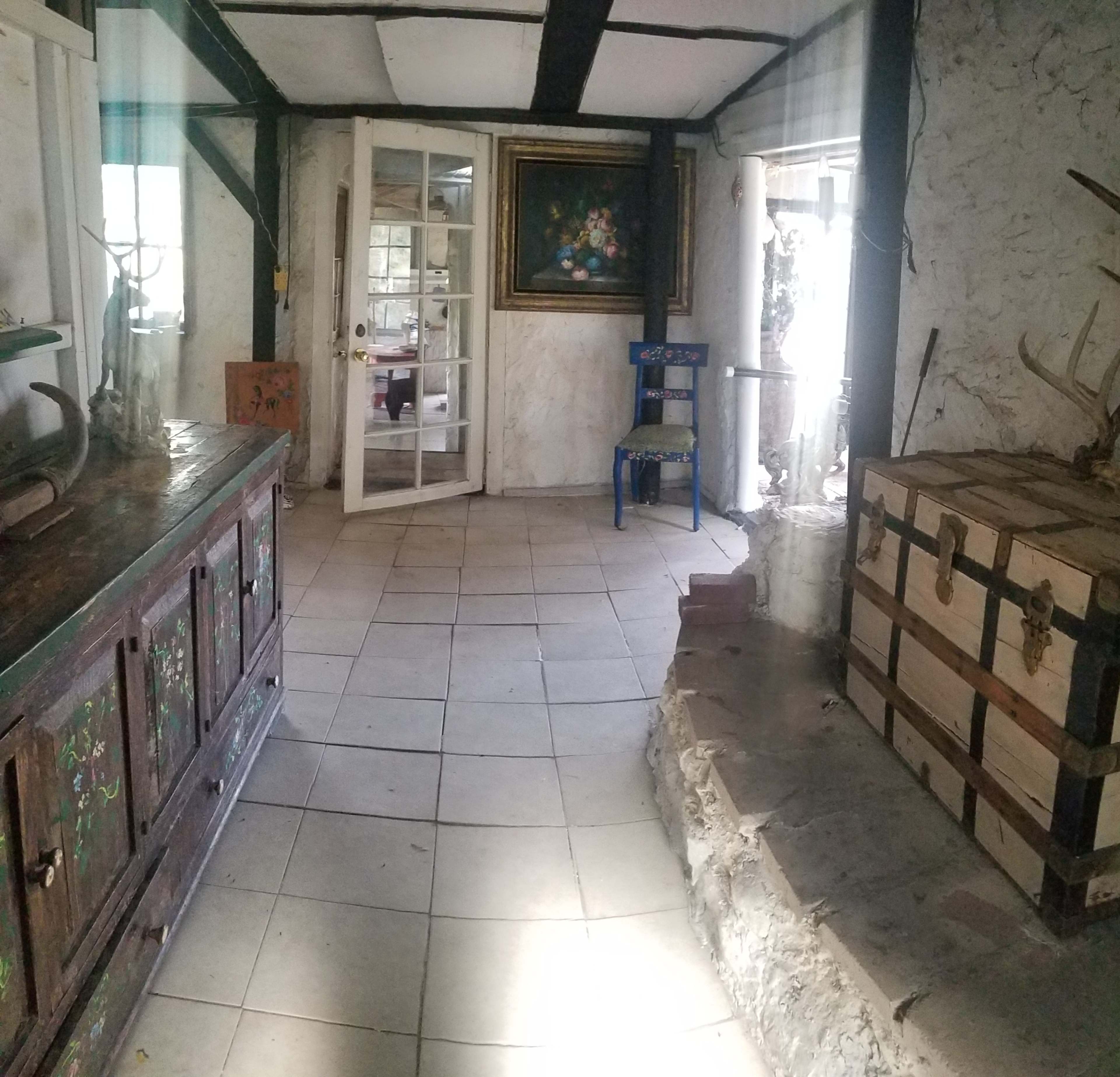 A spacious room with stone and plaster walls, featuring a wooden chest, a colorful chair, and a large painting on the wall.