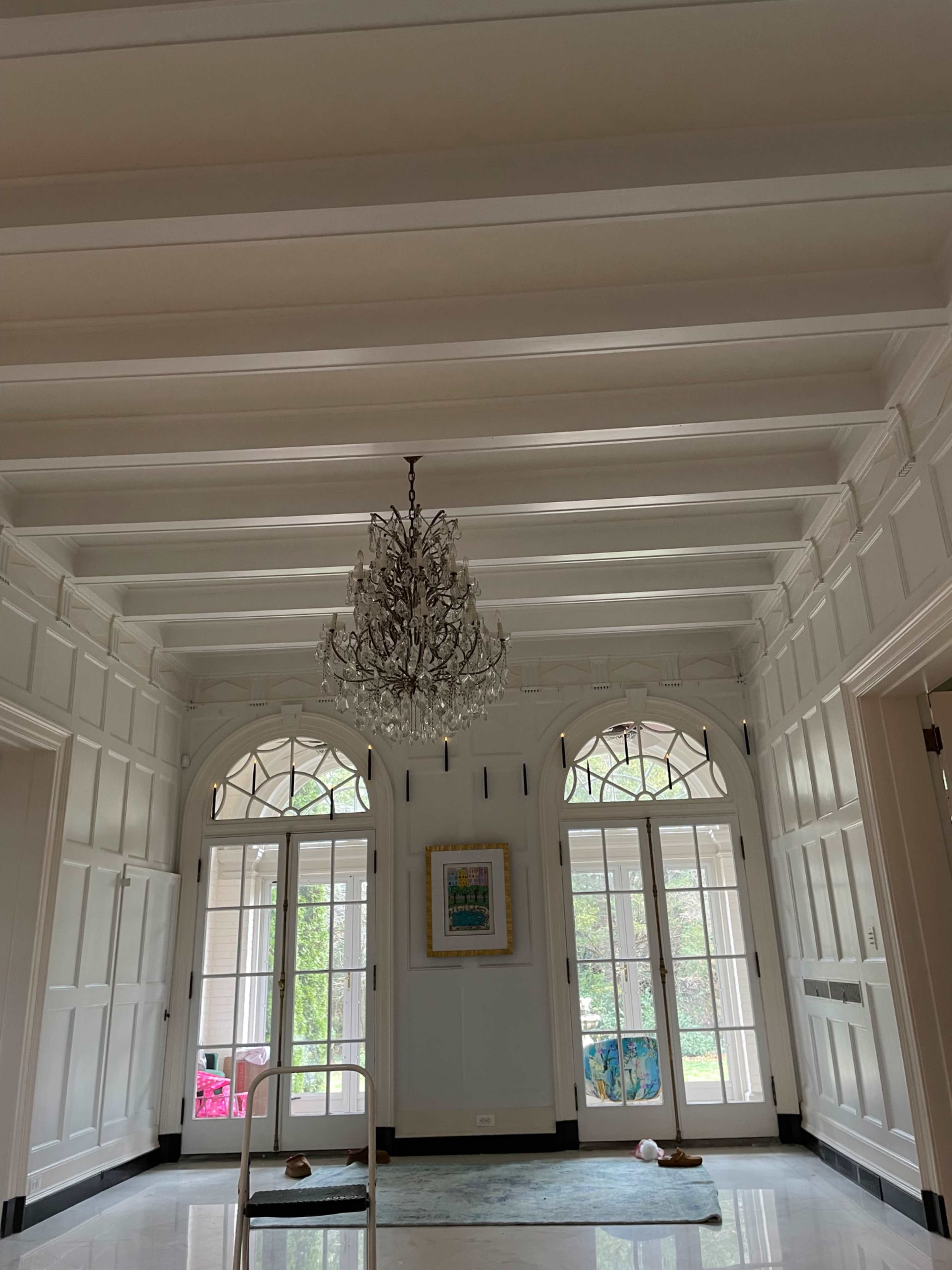 The image shows a spacious foyer with a chandelier, large windows, and white paneled walls.