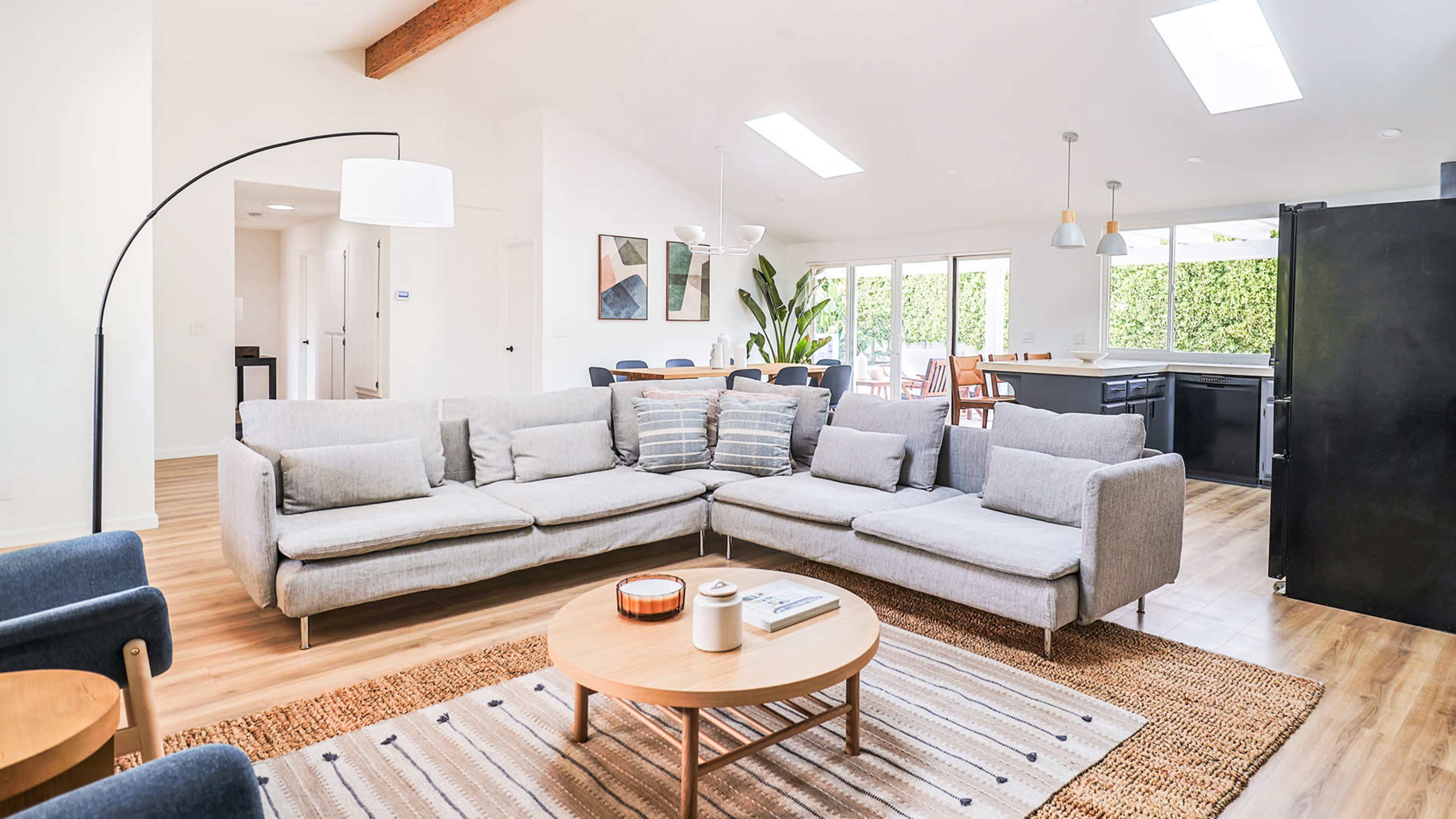 A modern living room with a large sectional sofa, a round coffee table, and an open layout leading to a dining area and kitchen.