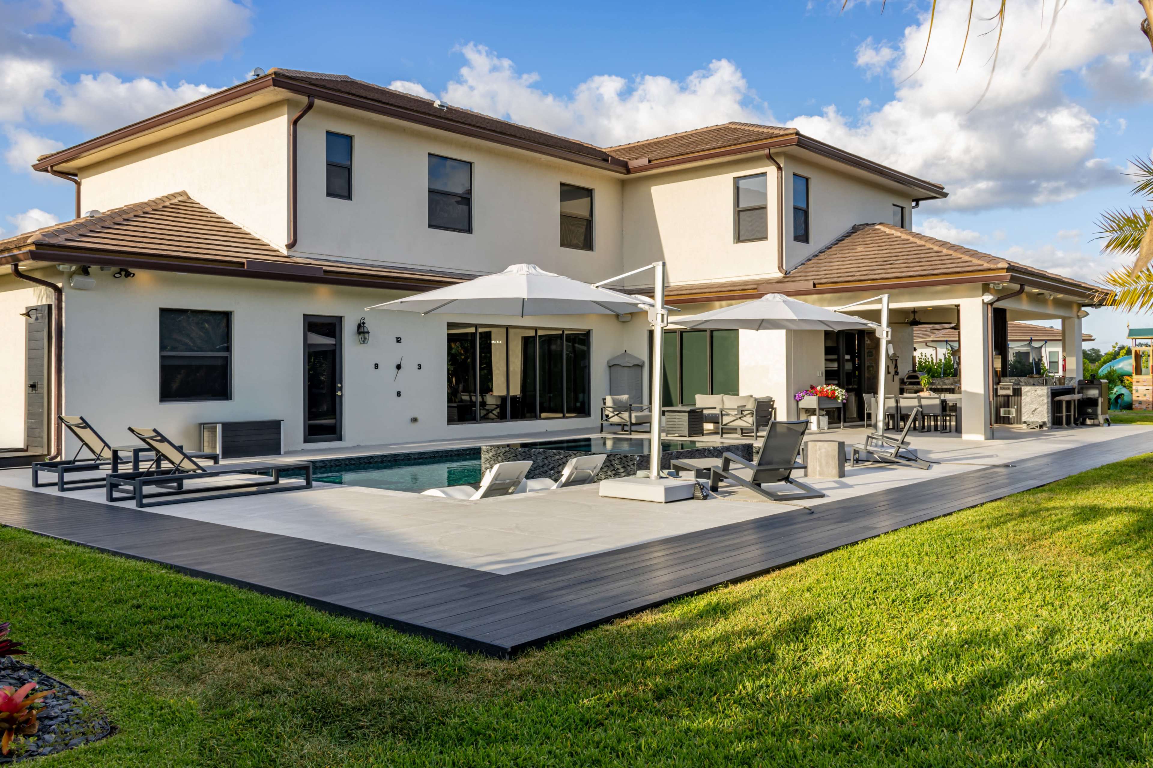 A modern two-story house features a swimming pool and patio area with lounge chairs and umbrellas.