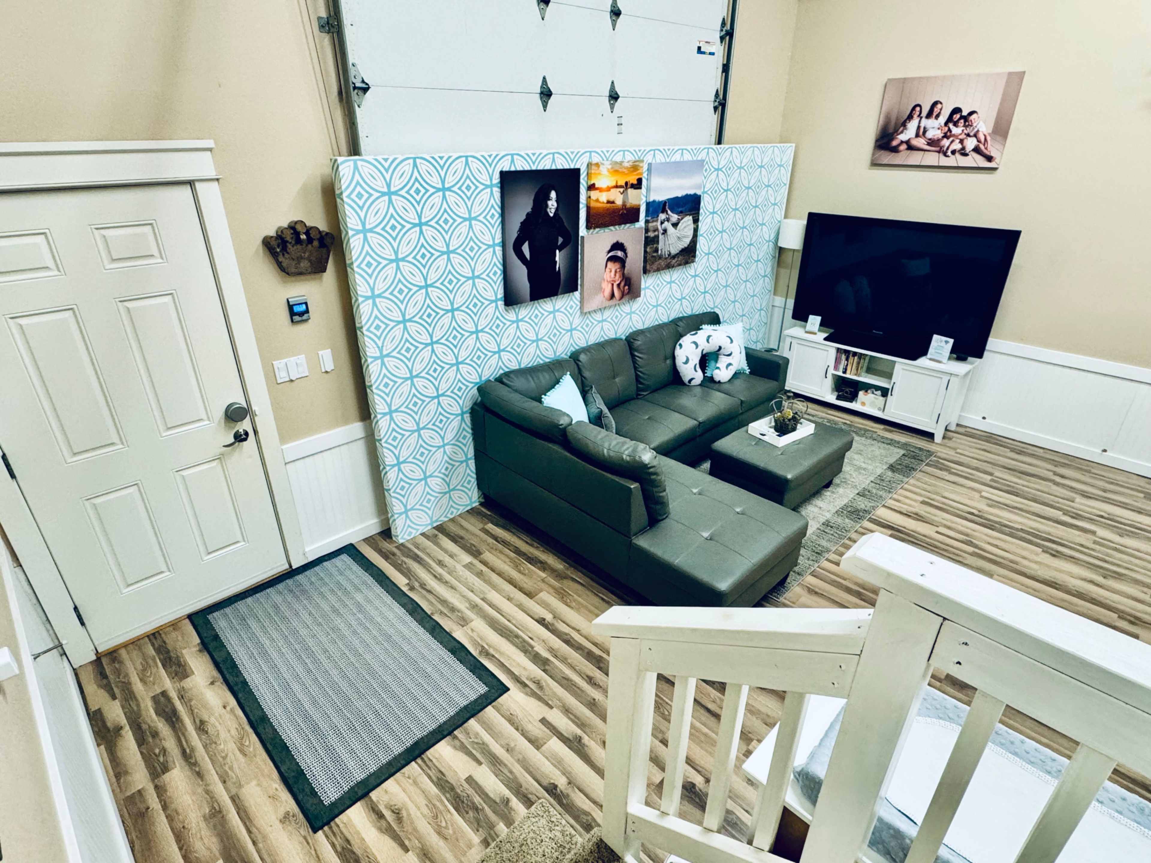 The image shows a living room with a sectional sofa, a large television on a stand, and decorative wall art against a patterned backdrop.