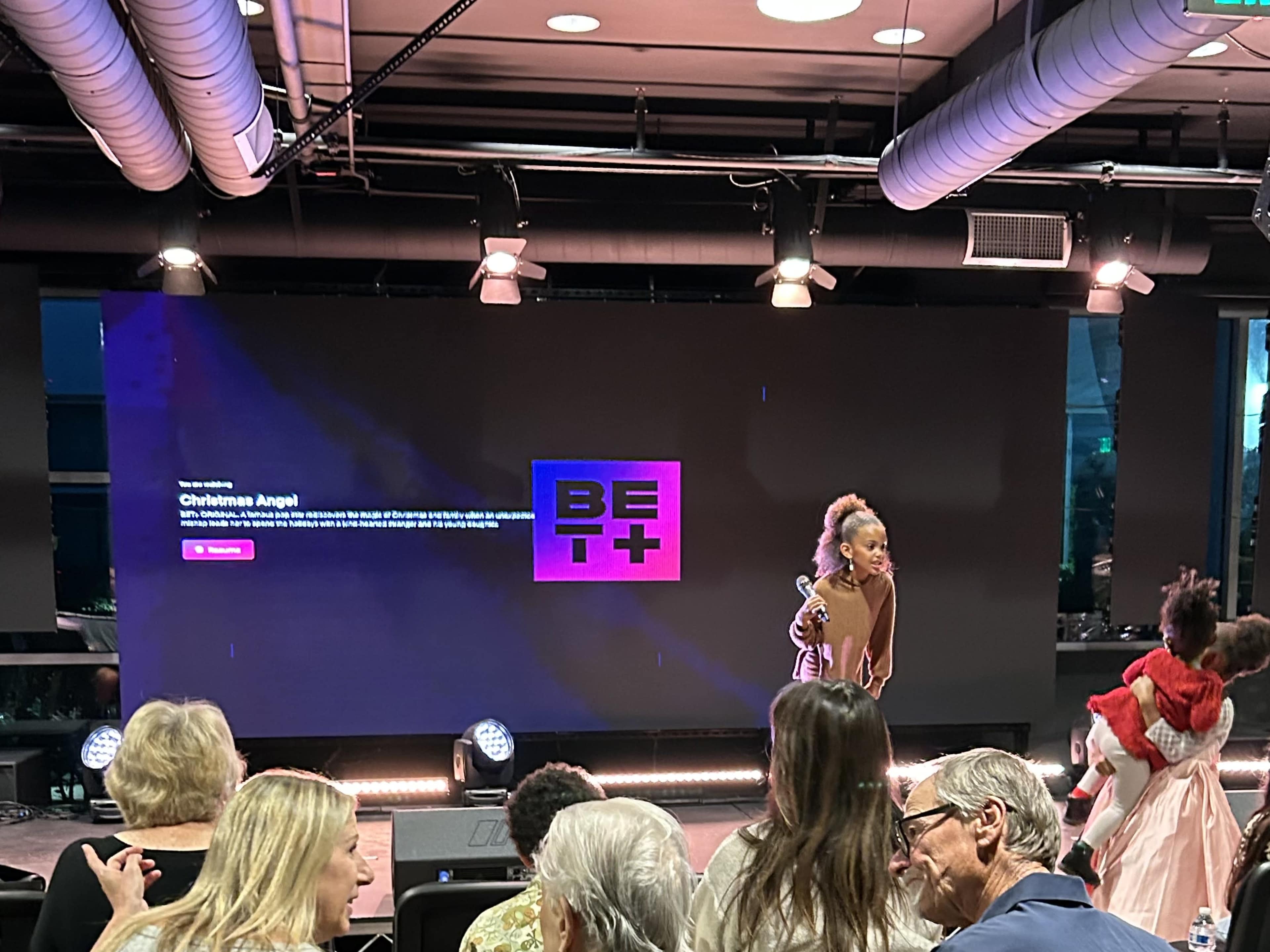 A young girl performs on stage while an audience watches in a venue with a large screen displaying the BET+ logo.