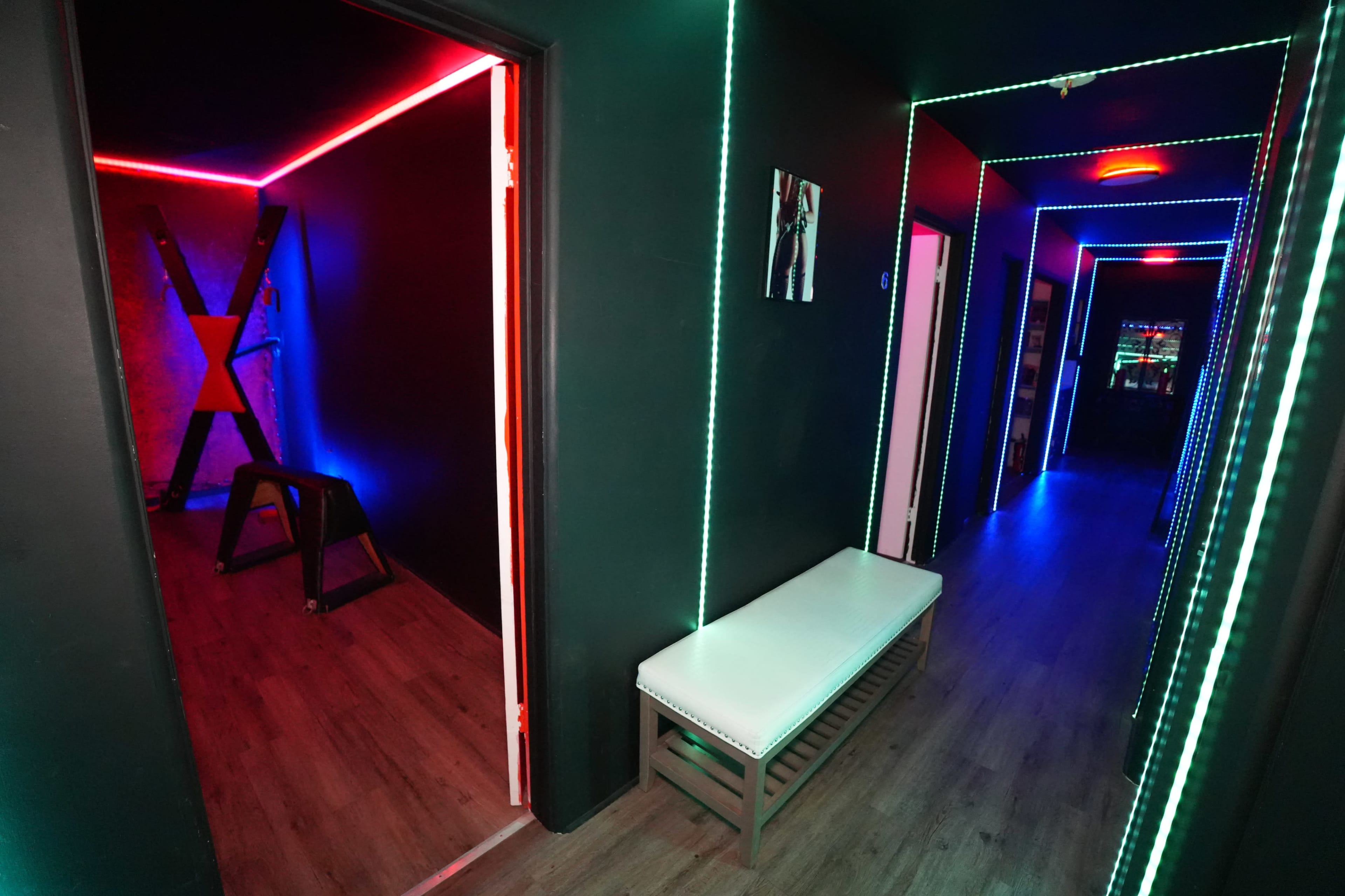 A dimly-lit hallway features blue and red LED strip lighting along the walls, with doors leading to rooms on either side and a white bench against one wall.