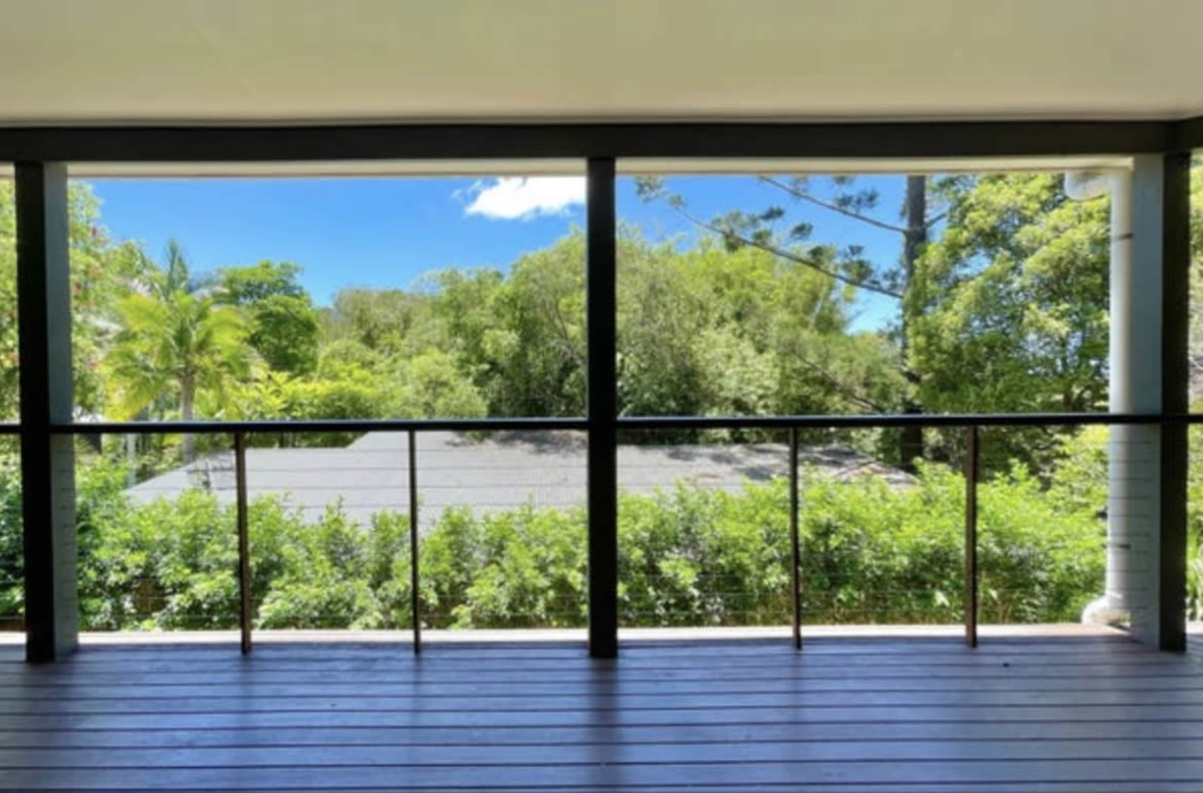 The image shows a balcony with a clear view of lush greenery and trees under a blue sky.