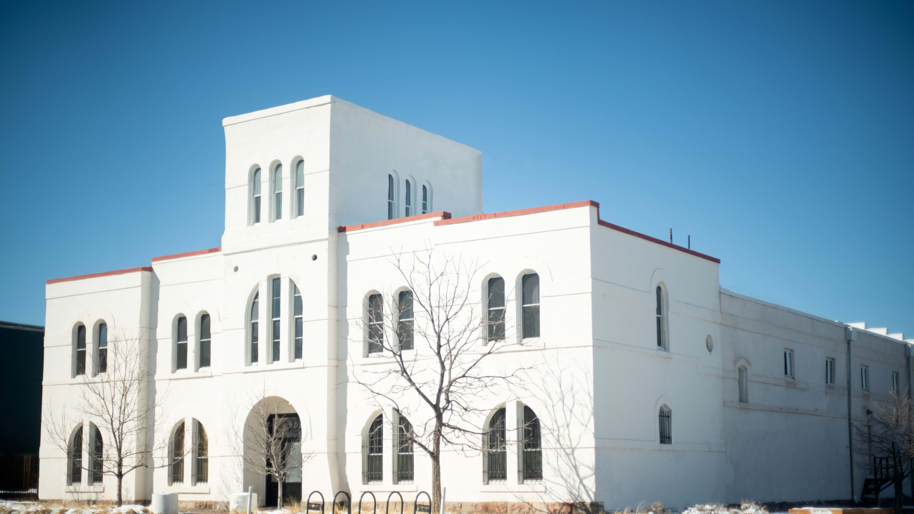 A large white building with distinctive arched windows and a flat roof under a clear blue sky.