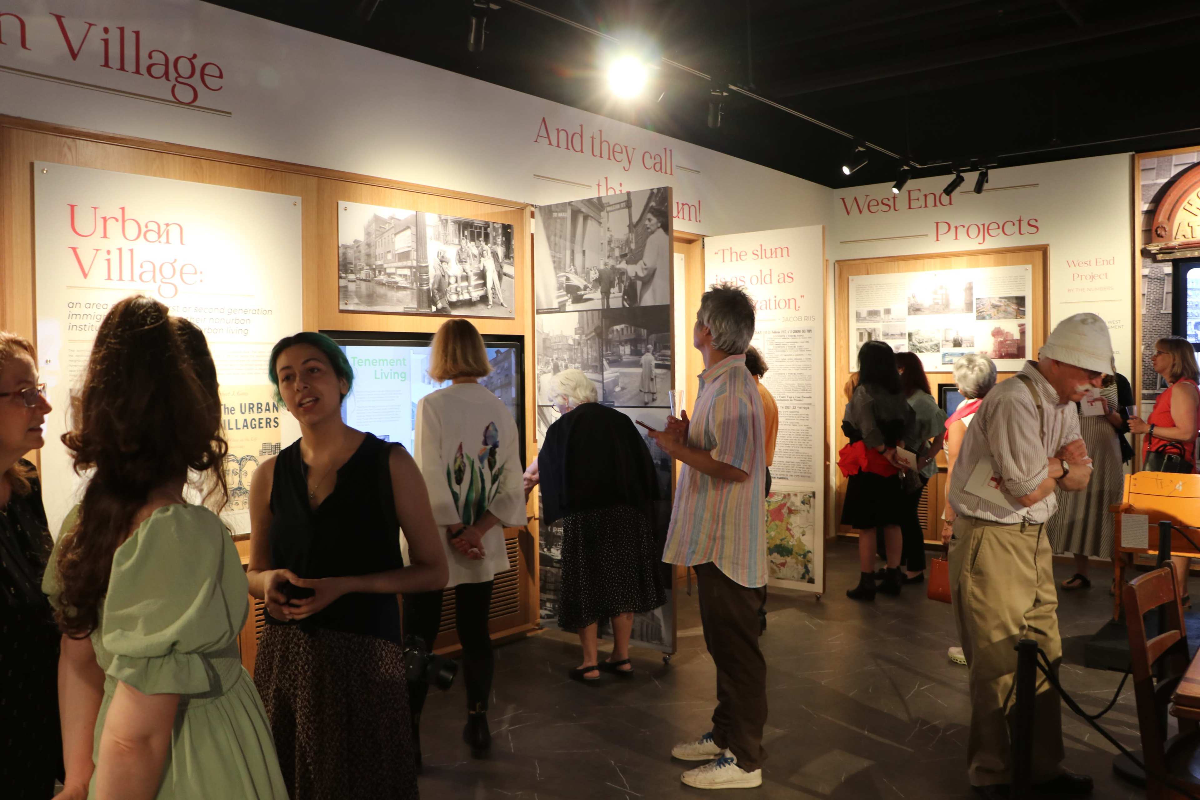 People are gathered in a museum exhibit featuring displays about urban communities, with informative panels and photographs on the walls.