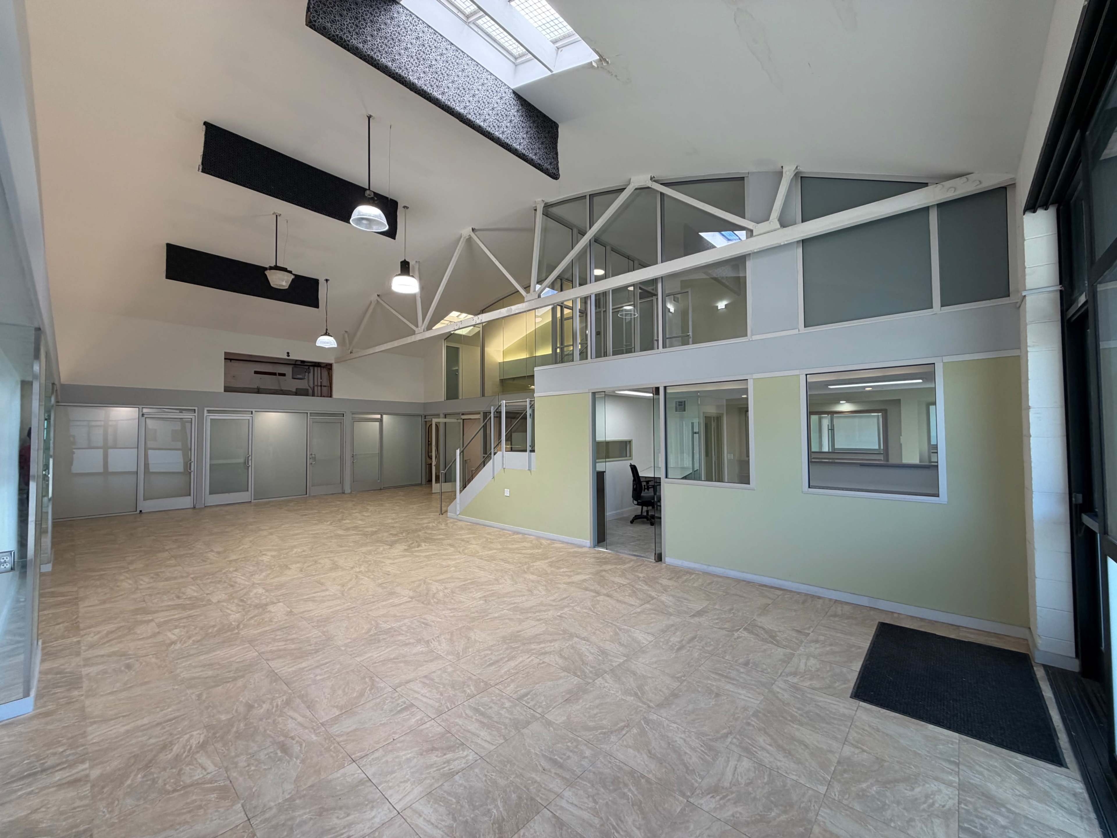 The image shows a spacious office interior with high ceilings, large windows, and divided workspaces.
