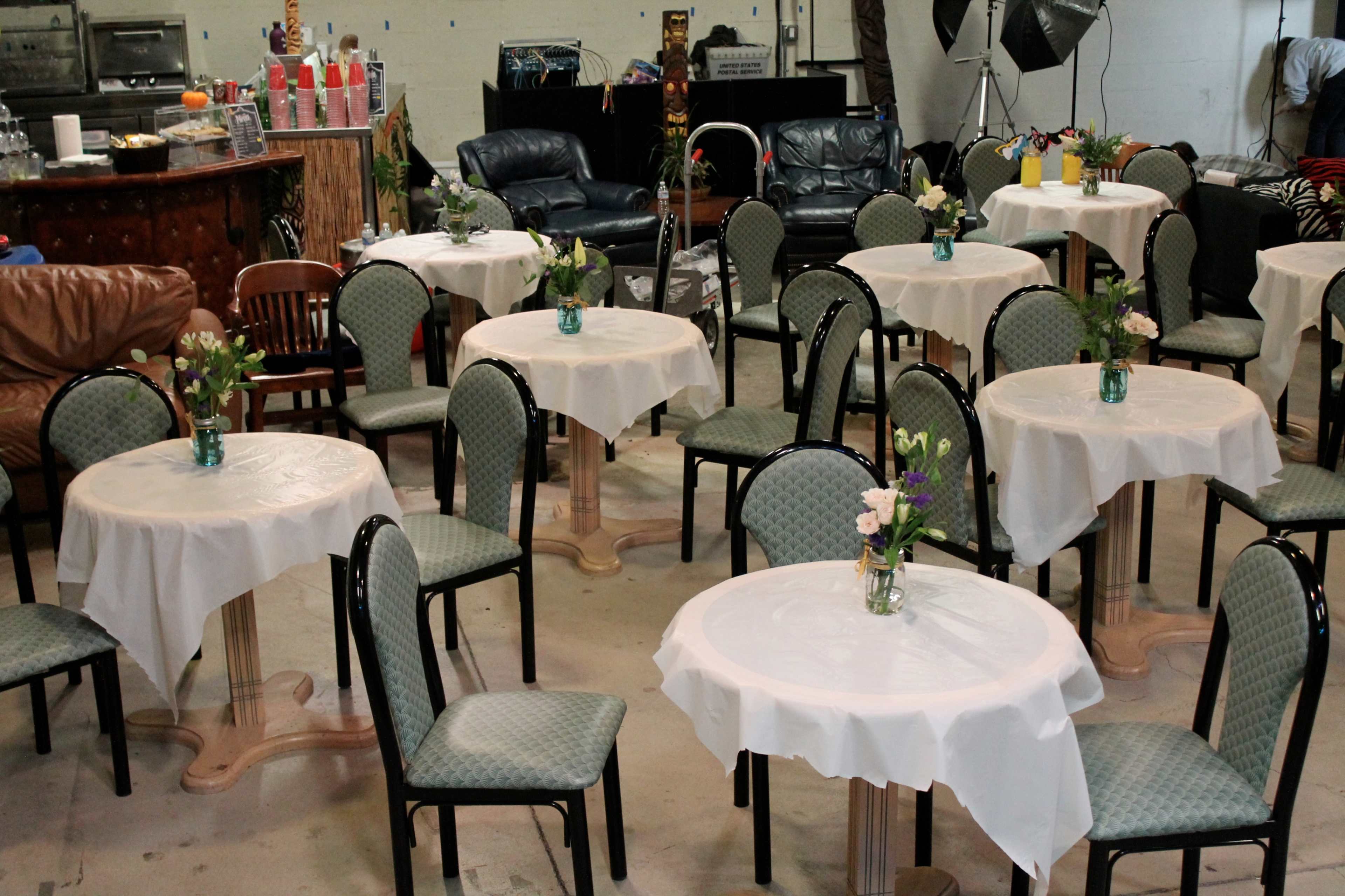 A seating area with small tables covered in white tablecloths, surrounded by chairs, and decorated with flower arrangements in glass vases.