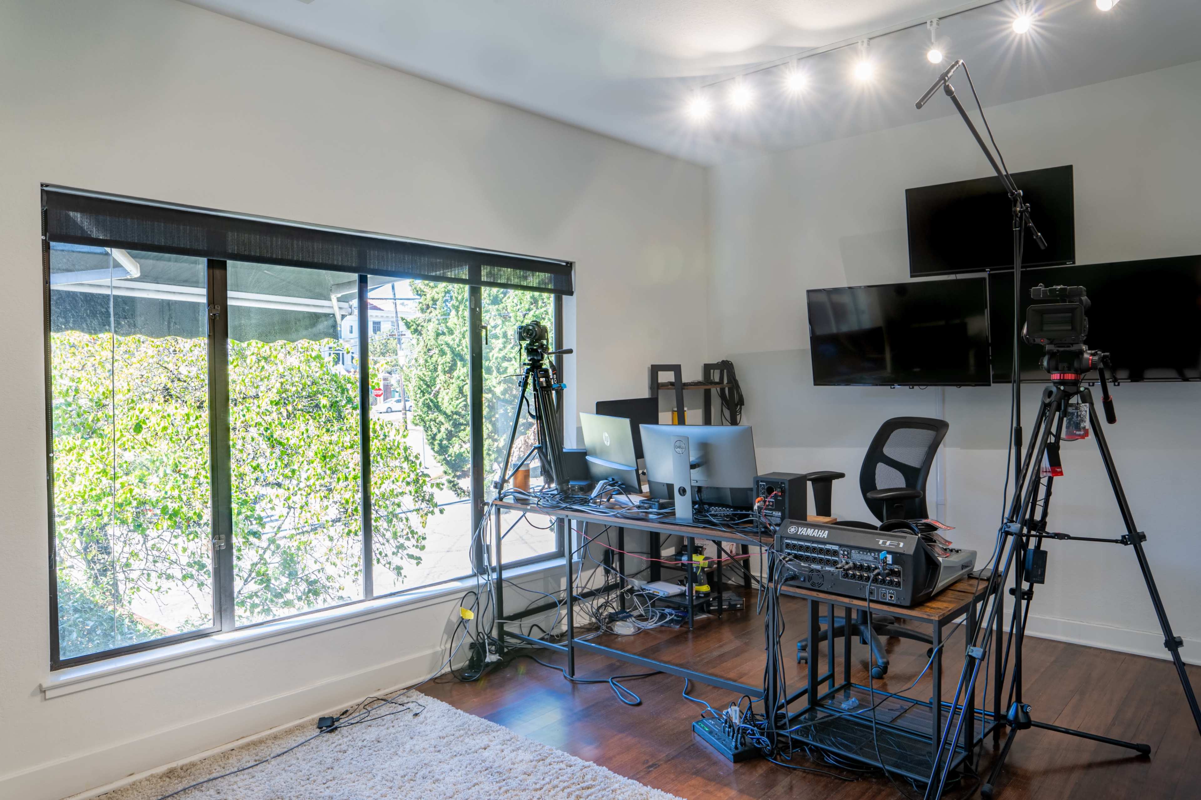 A modern office space featuring a desk with computers and camera equipment set up near a large window.