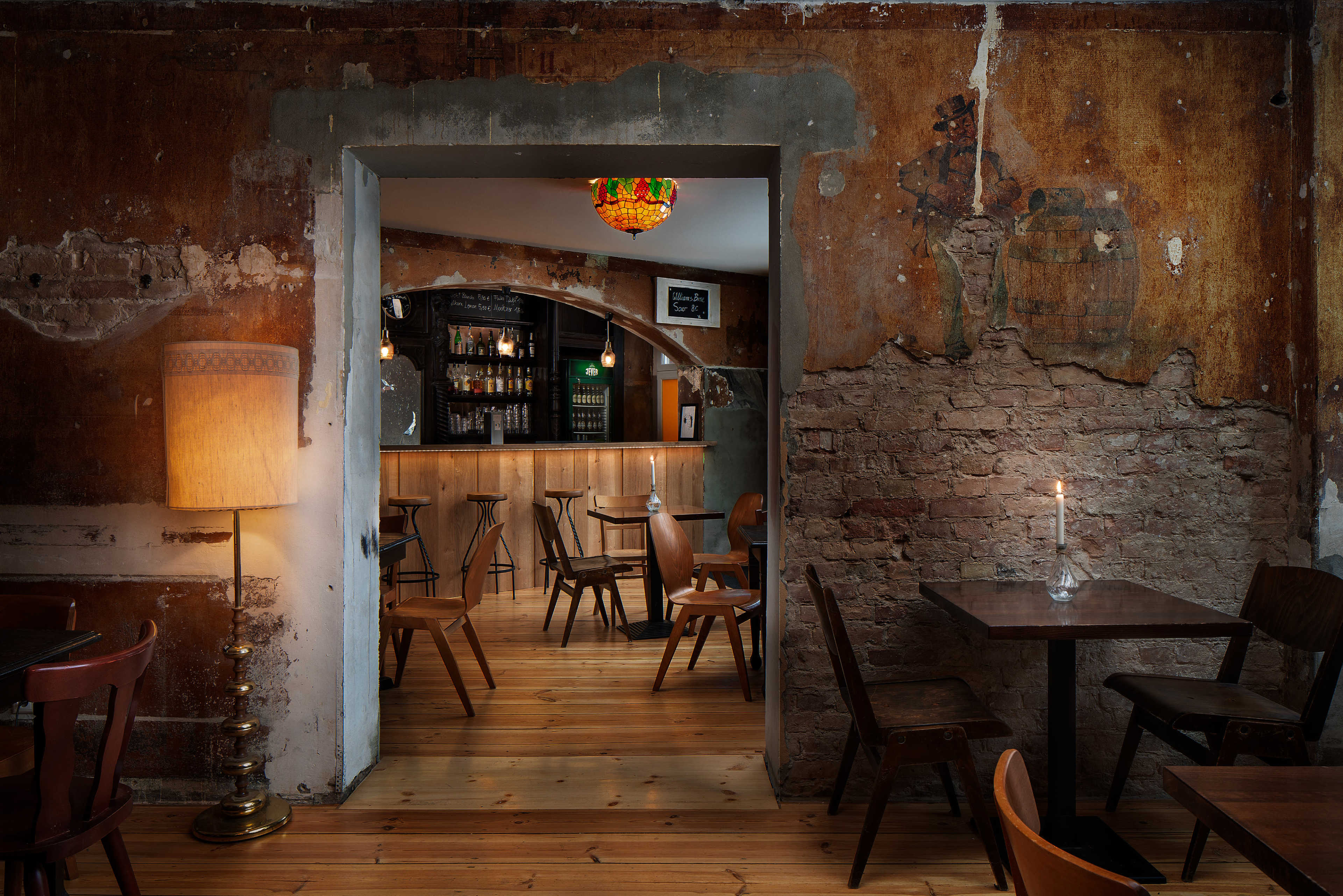 A dimly lit restaurant features rustic decor with exposed brick walls, wooden floors, and a bar area visible through an archway.