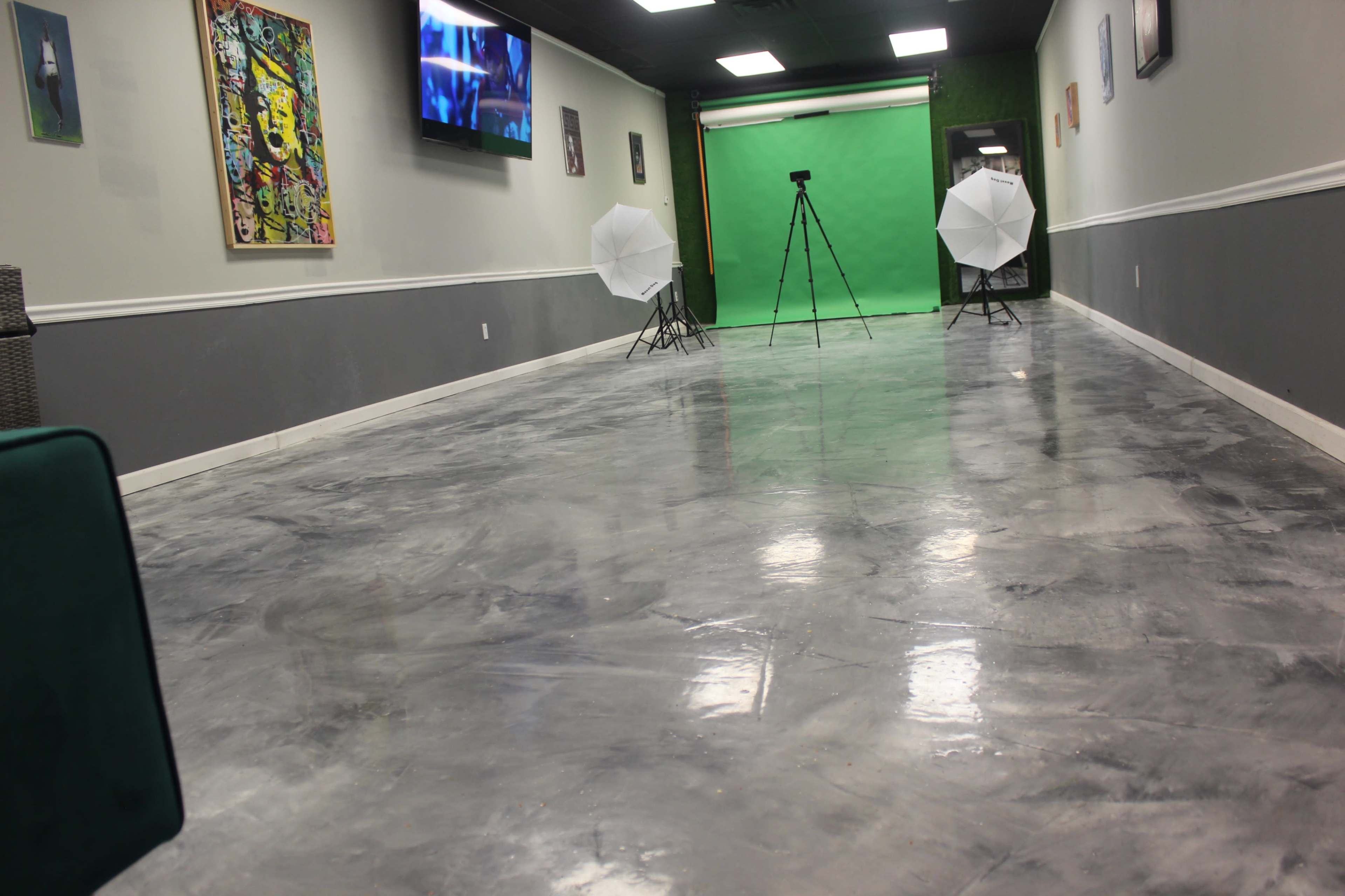The image shows a spacious room with a polished concrete floor, two white umbrella lights set up on tripods, and a green backdrop along one wall.