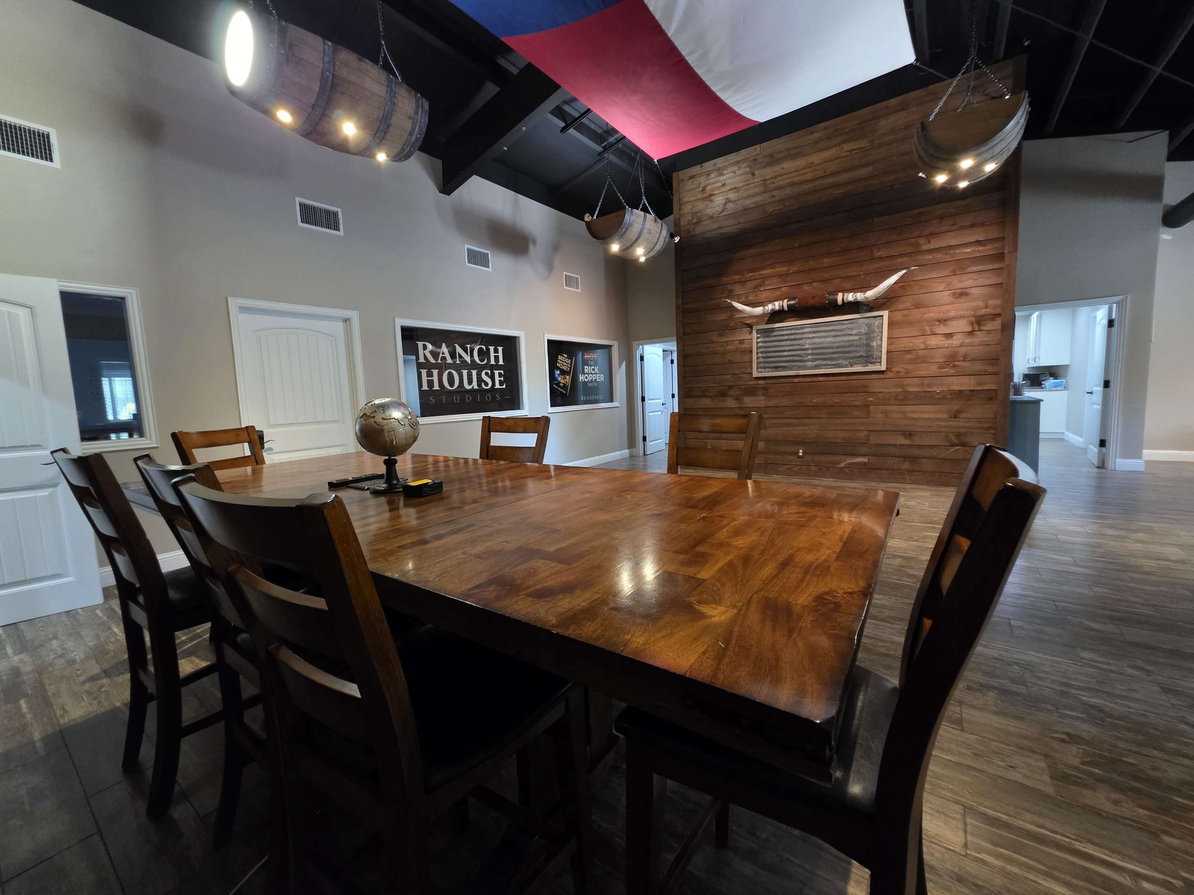 The image shows a dining area with a large wooden table surrounded by chairs, a decorative globe on the table, and a rustic wooden wall with mounted decor.