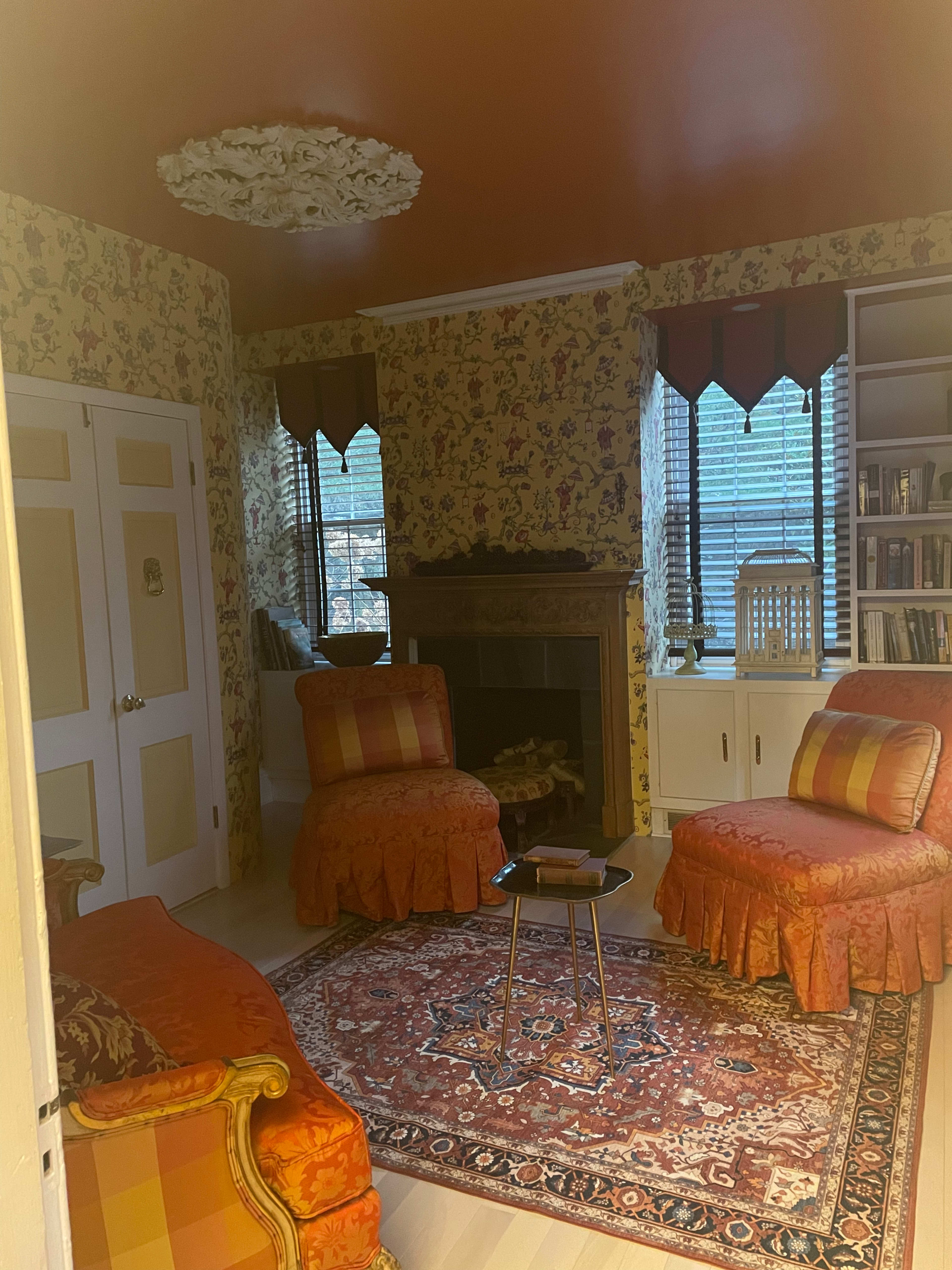 A cozy sitting room features two patterned armchairs, a small table between them, and a fireplace flanked by built-in bookshelves, all surrounded by floral wallpaper.