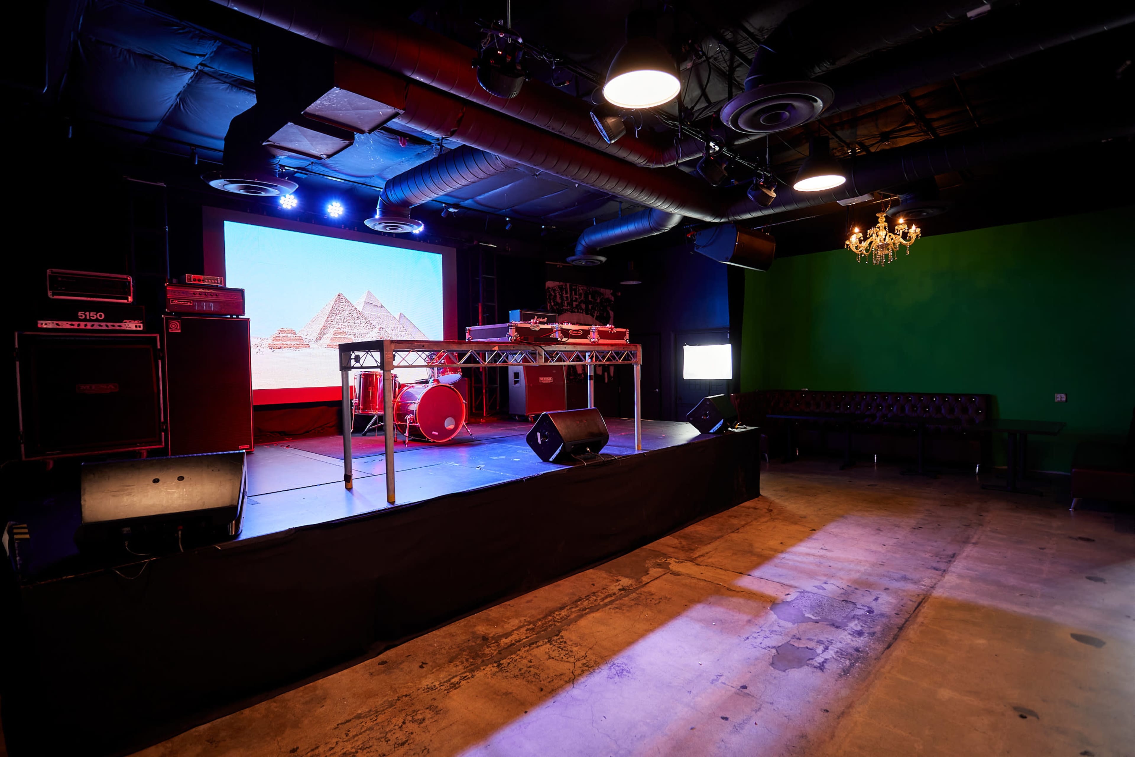 A stage set up for a performance with musical instruments, amplifiers, and a large screen displaying pyramids in a dimly lit venue.