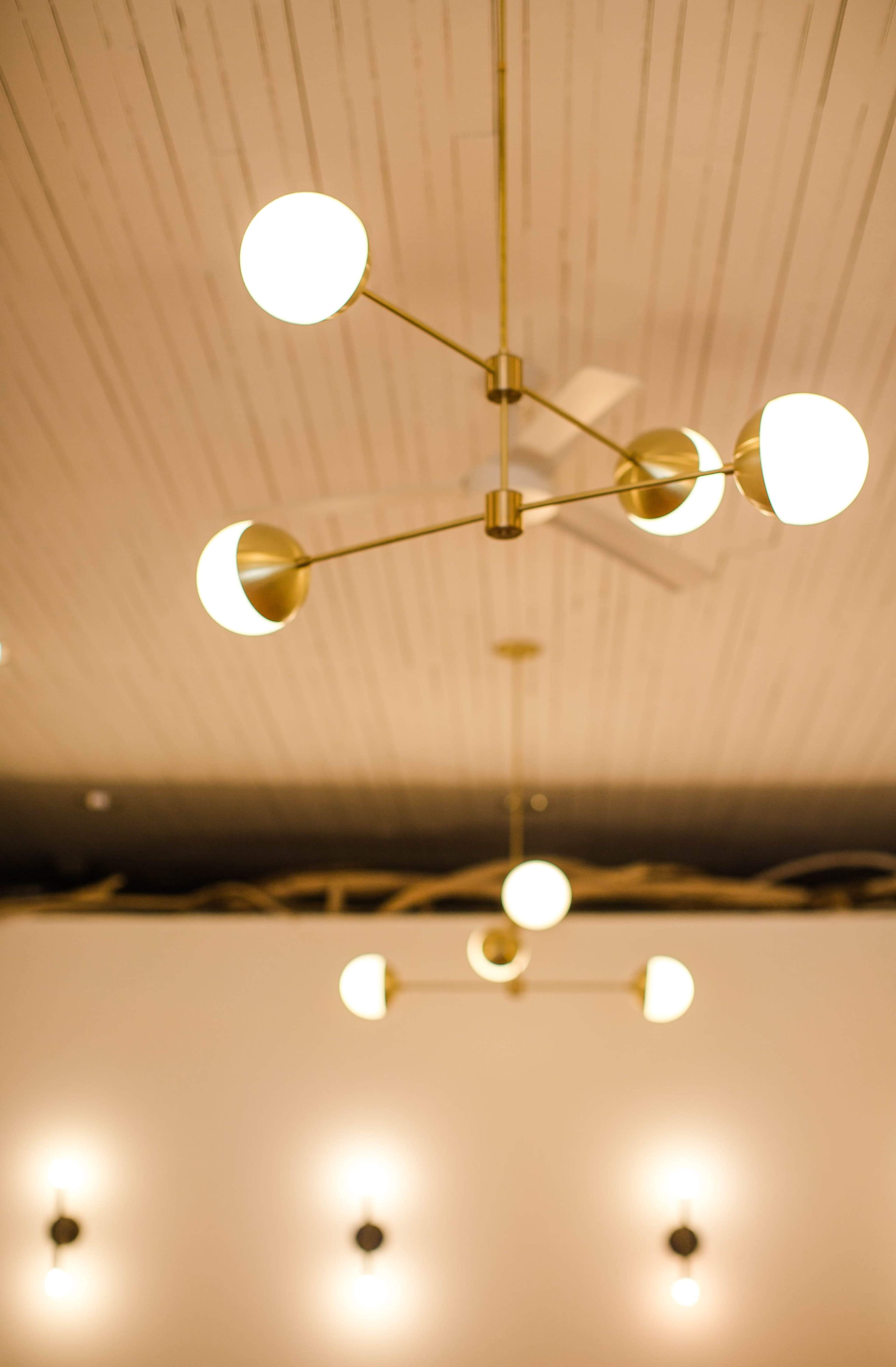 The image shows a modern chandelier with multiple spherical lights suspended from a gold metal structure against a light-colored ceiling.