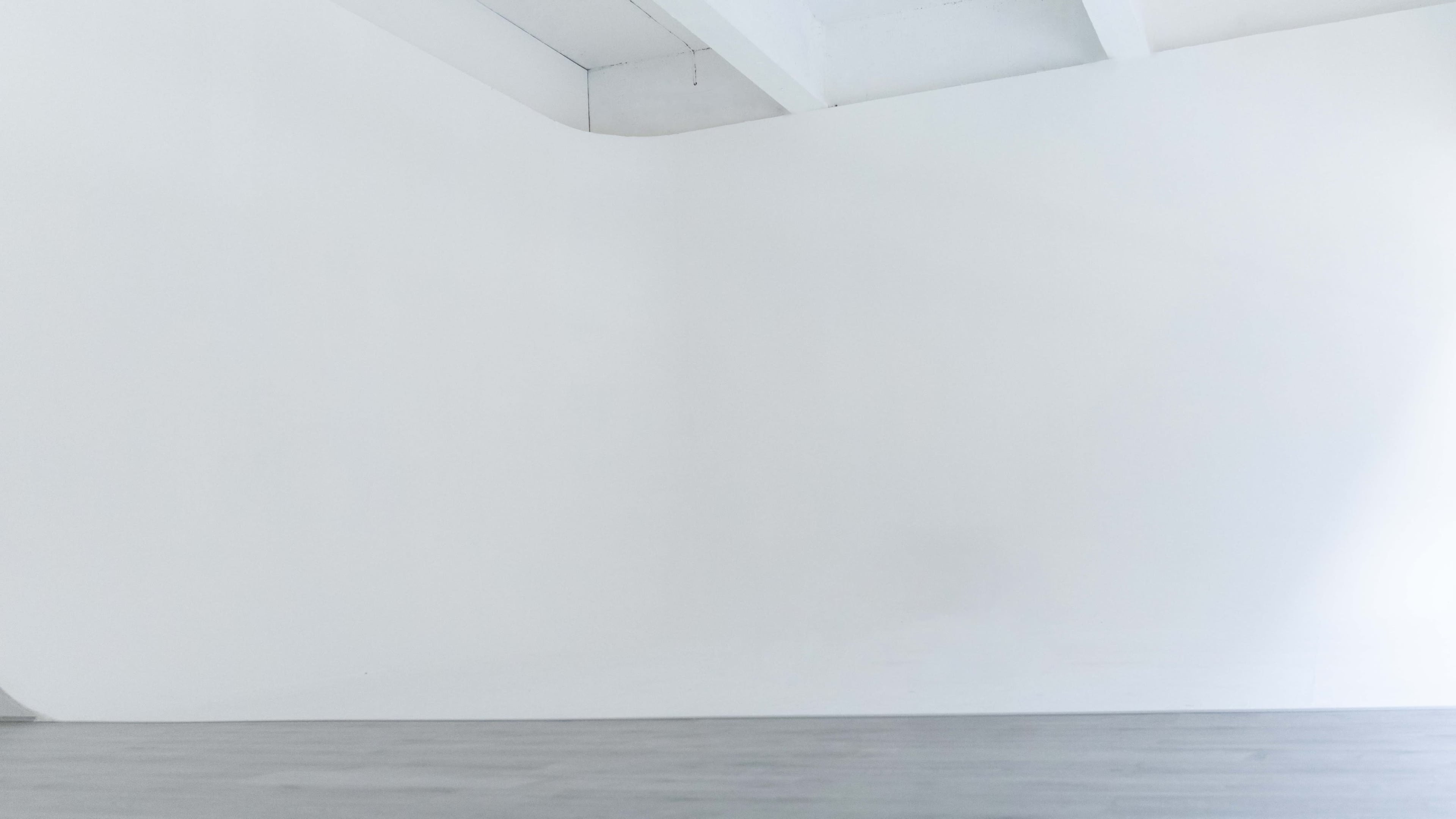 A minimalist interior space with a plain white wall and a gray wooden floor.