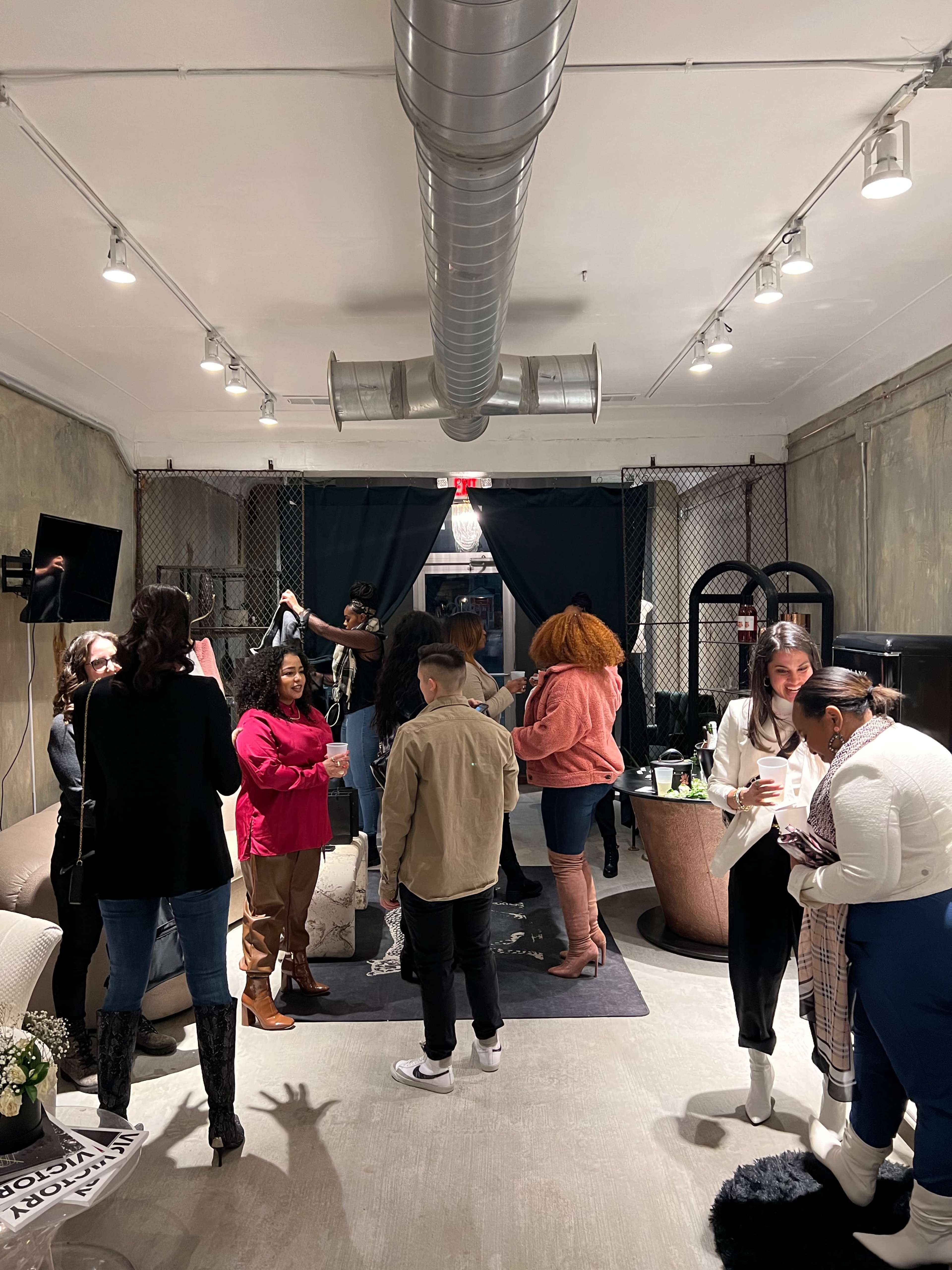 A group of people gathers in a stylishly decorated indoor space with exposed walls and various seating arrangements.
