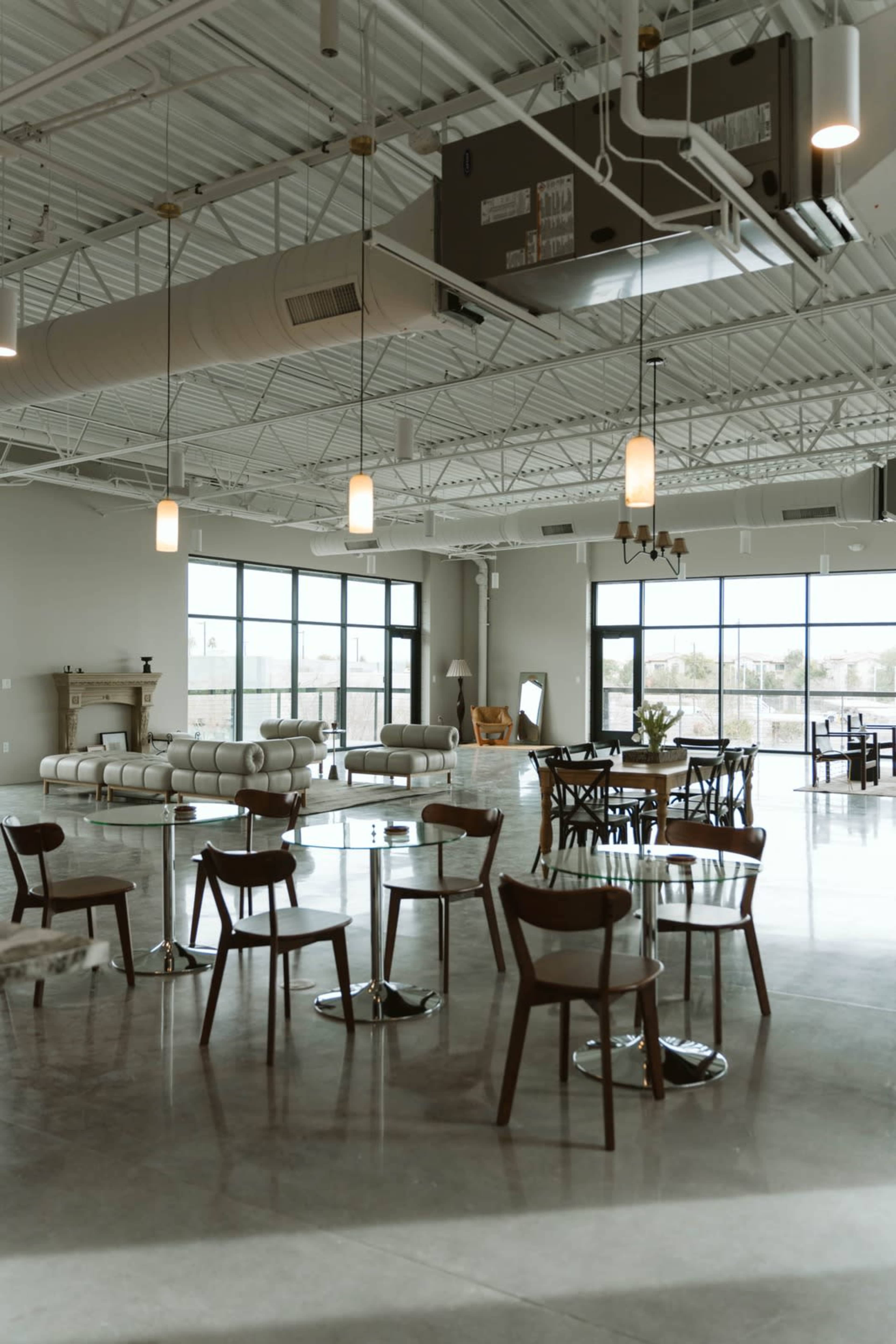 The image shows an open and airy interior space with modern furniture, large windows, and industrial-style ceilings.