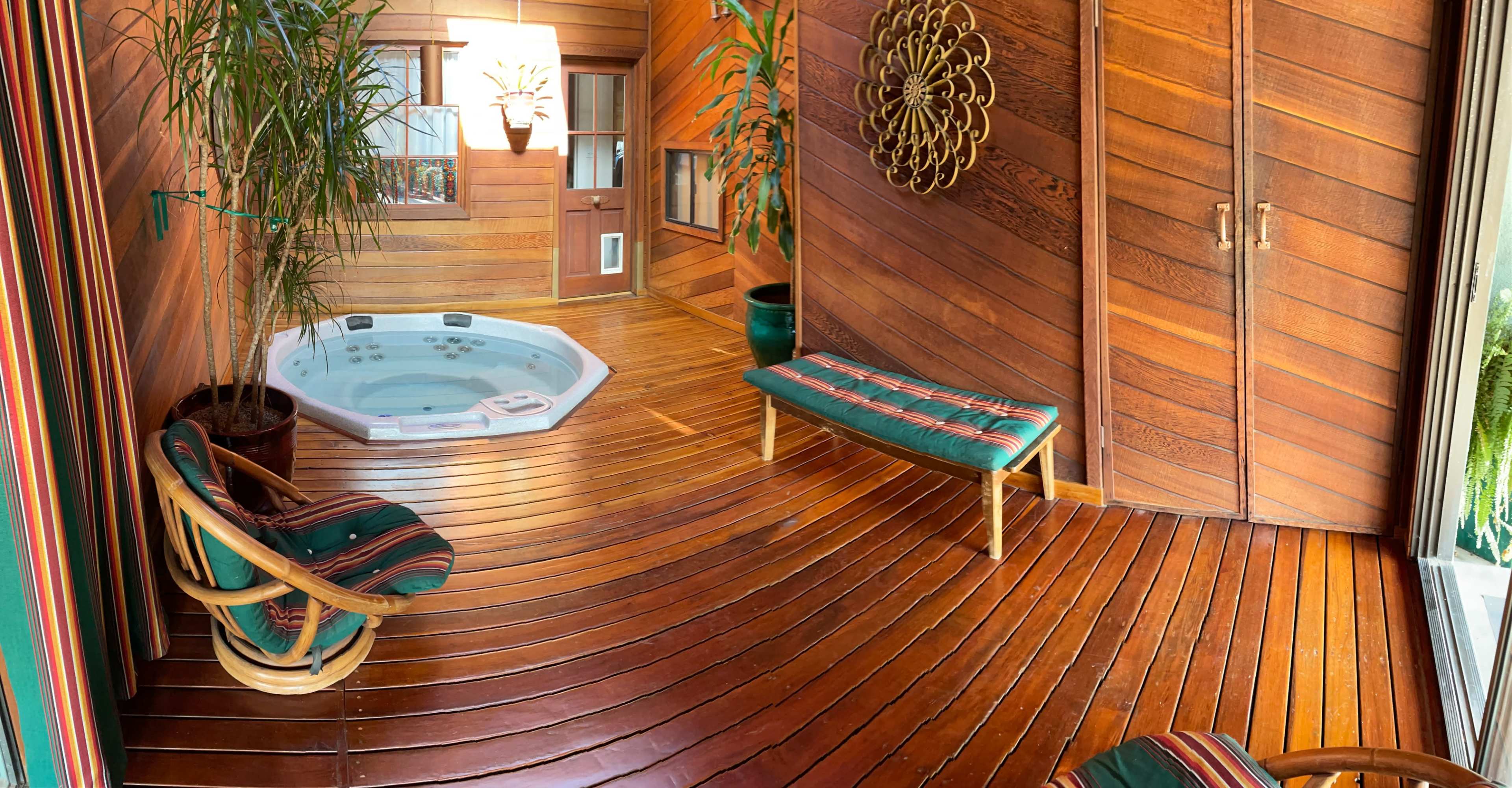 A wooden interior room with a jacuzzi, two striped lounge chairs, and potted plants.
