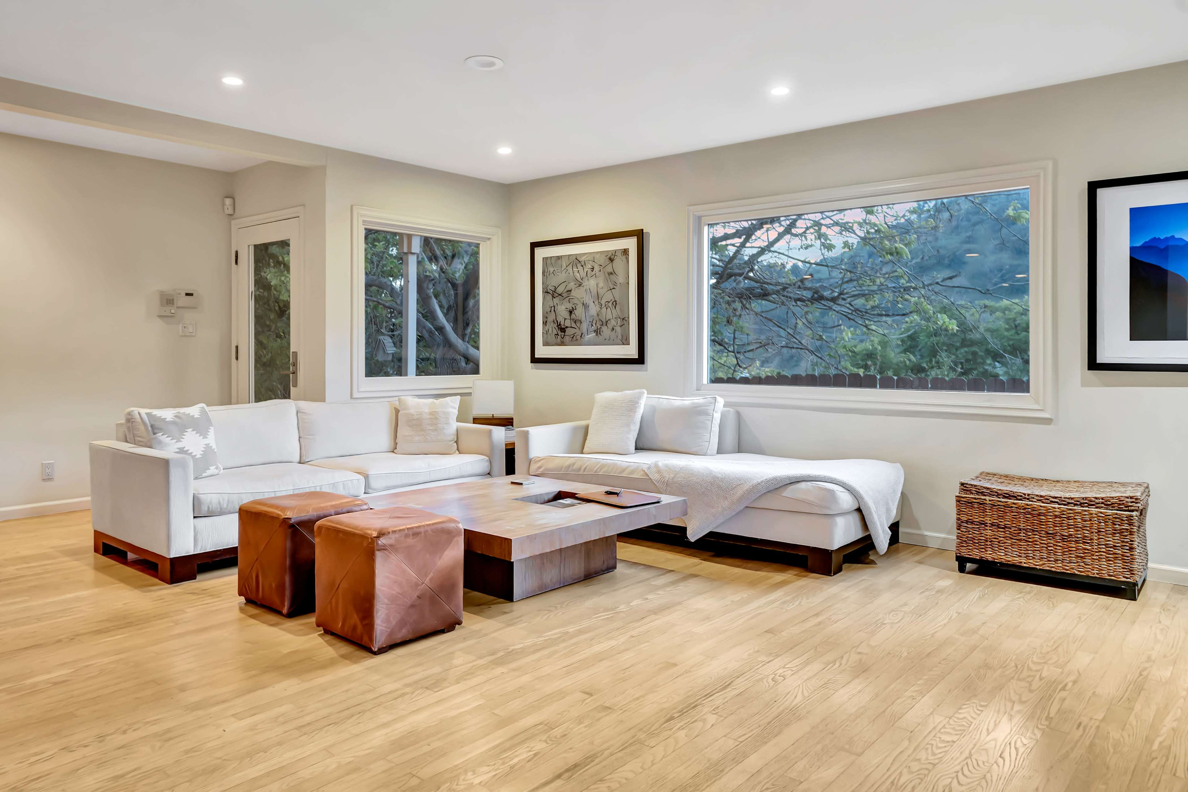 The room features a light-colored living area with a sectional sofa, wooden coffee table, and natural light coming through large windows.