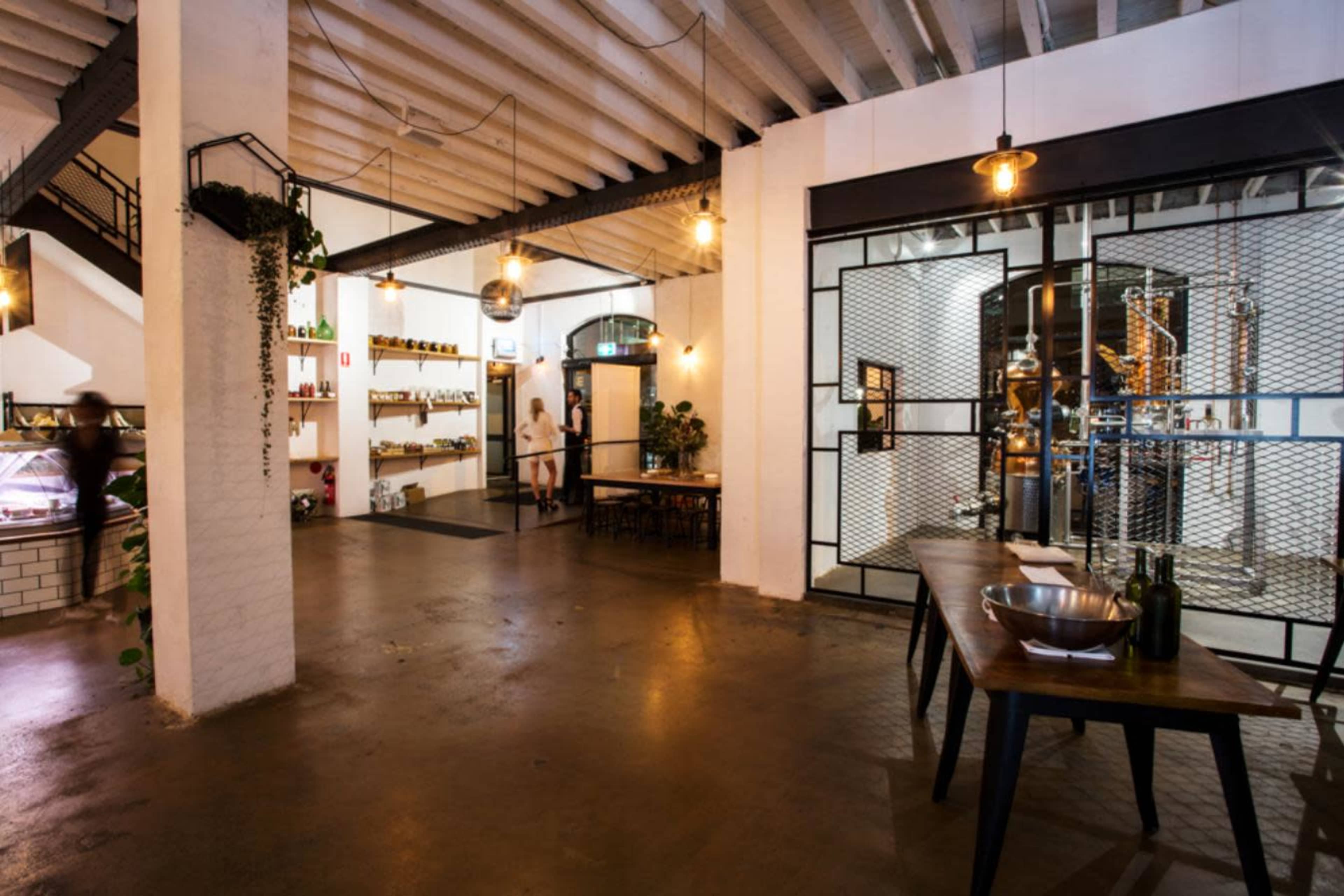 A modern, industrial-style restaurant interior with exposed beams, a dining area, and visible kitchen equipment behind a glass partition.