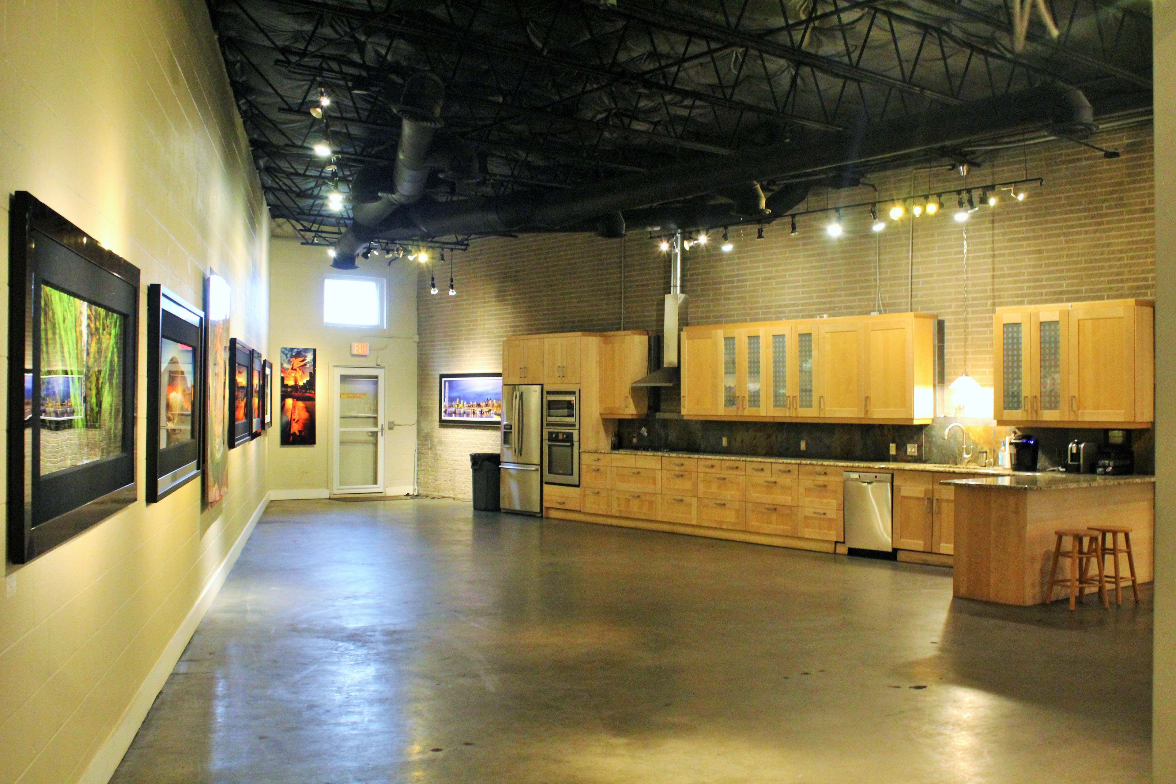 A large, well-lit art gallery with a kitchen area on one side and framed photographs displayed on the walls.