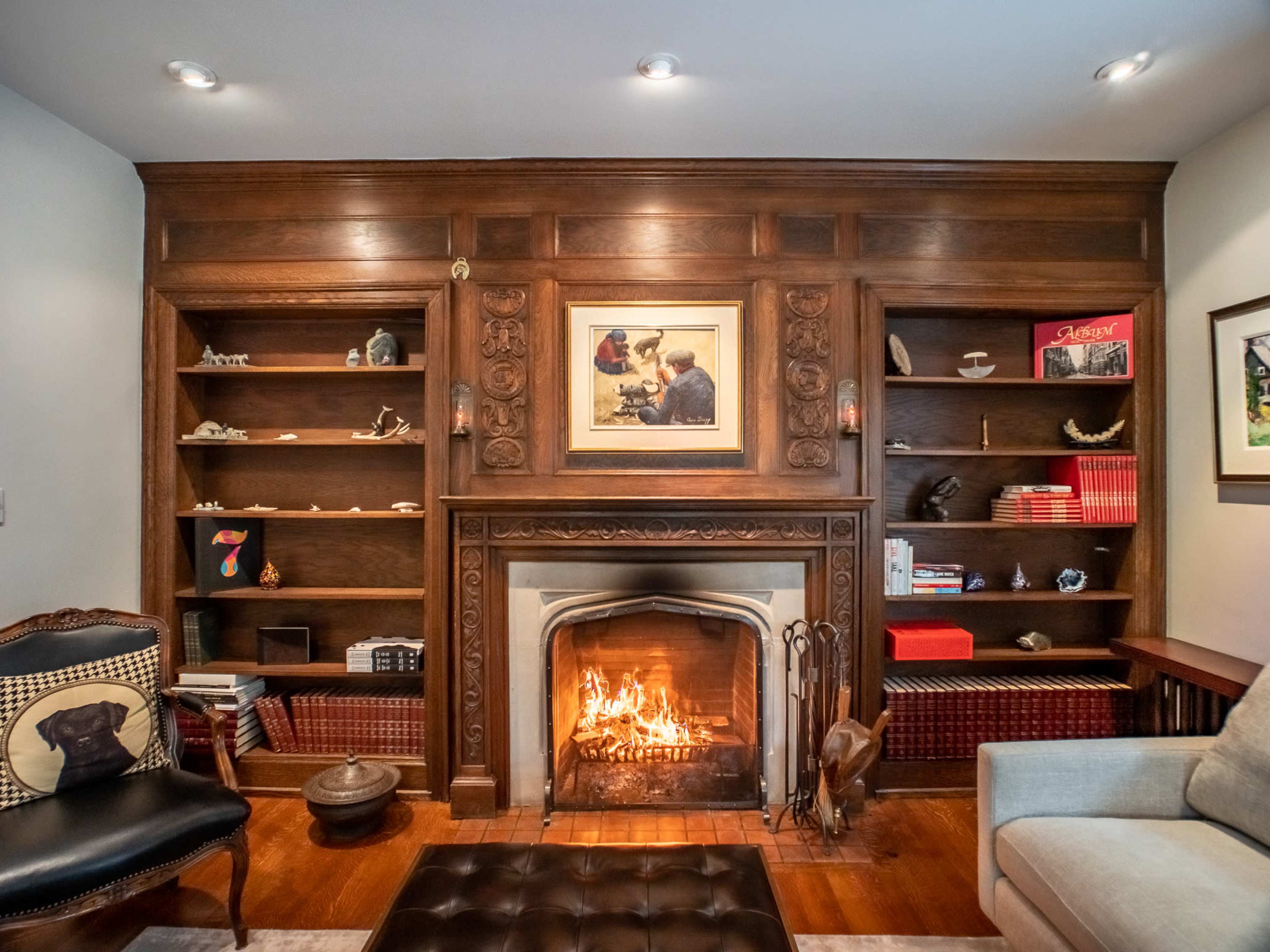 A cozy living room features a wooden bookshelf, a fireplace with an active flame, and a mix of upholstered furniture.