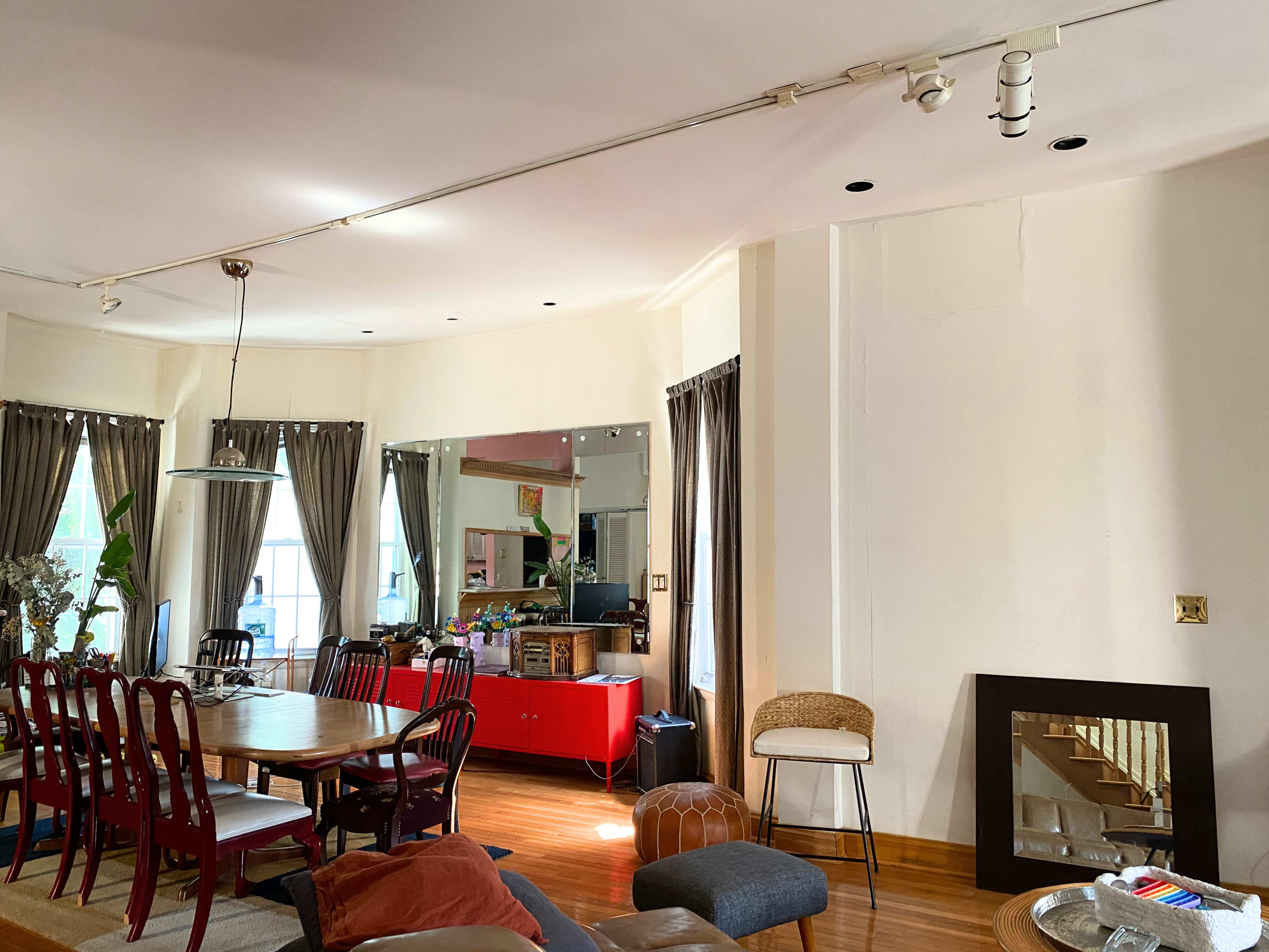 A spacious dining area with a large table, red cabinetry, mirror reflections, and chairs arranged around the room.