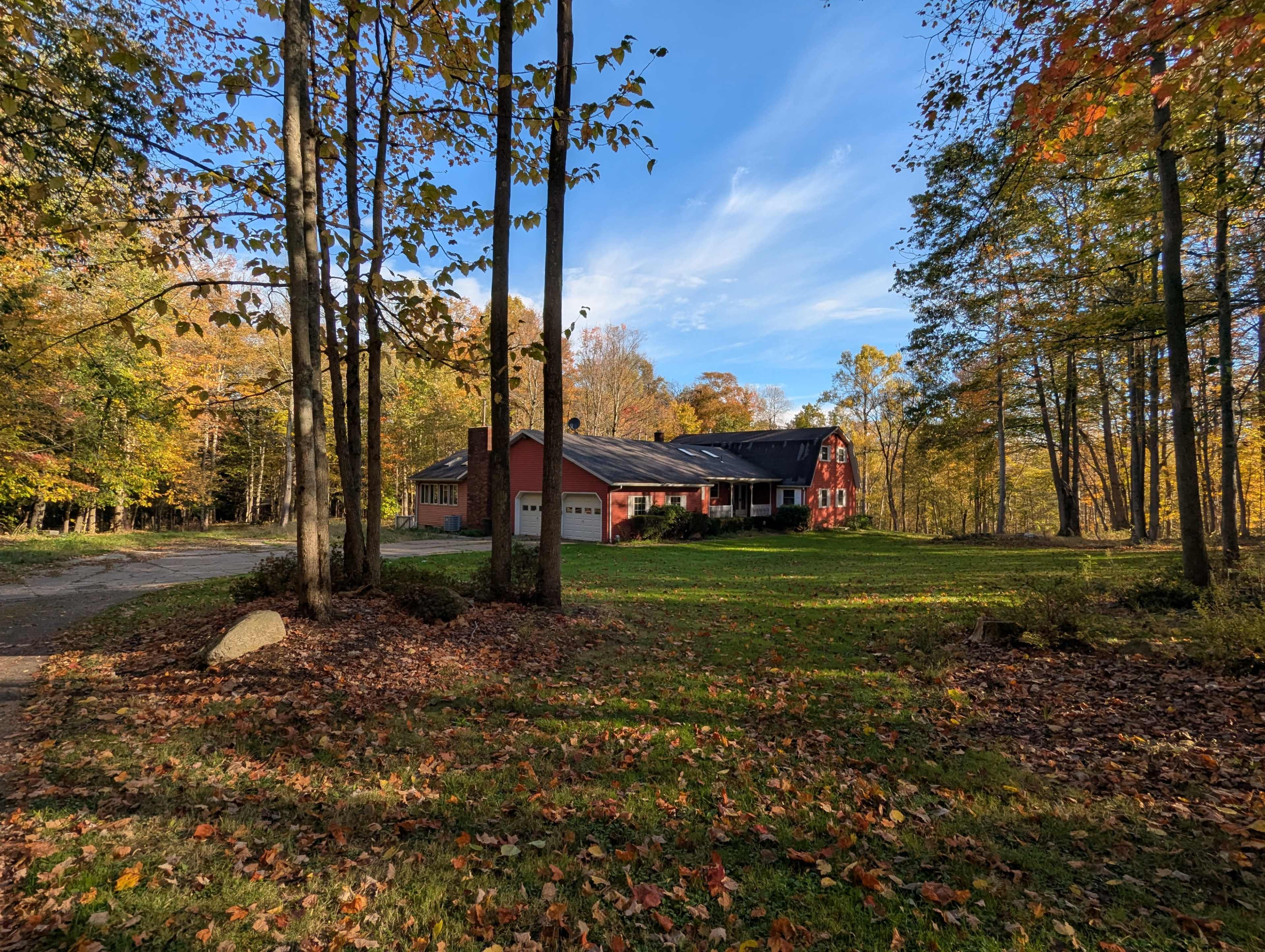 A red house with a garage is surrounded by trees and autumn foliage on a clear day.