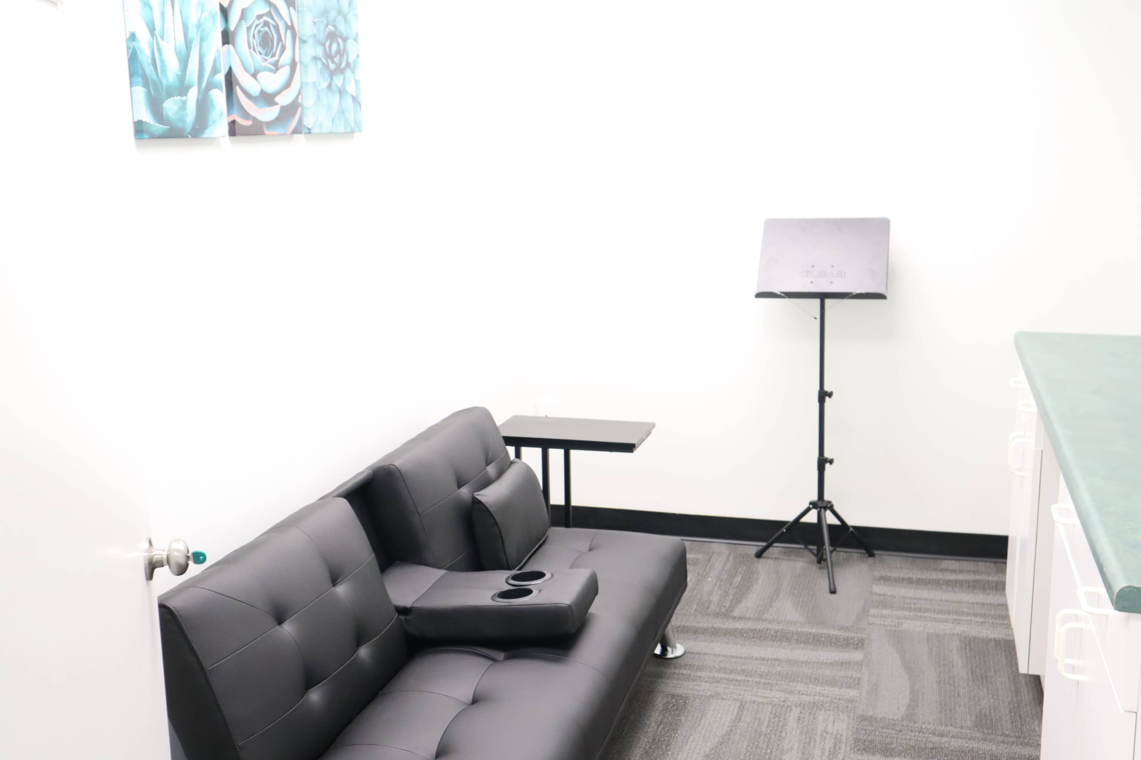 A minimalistic room with a black sofa, a small side table, and a music stand against a white wall adorned with blue floral artwork.