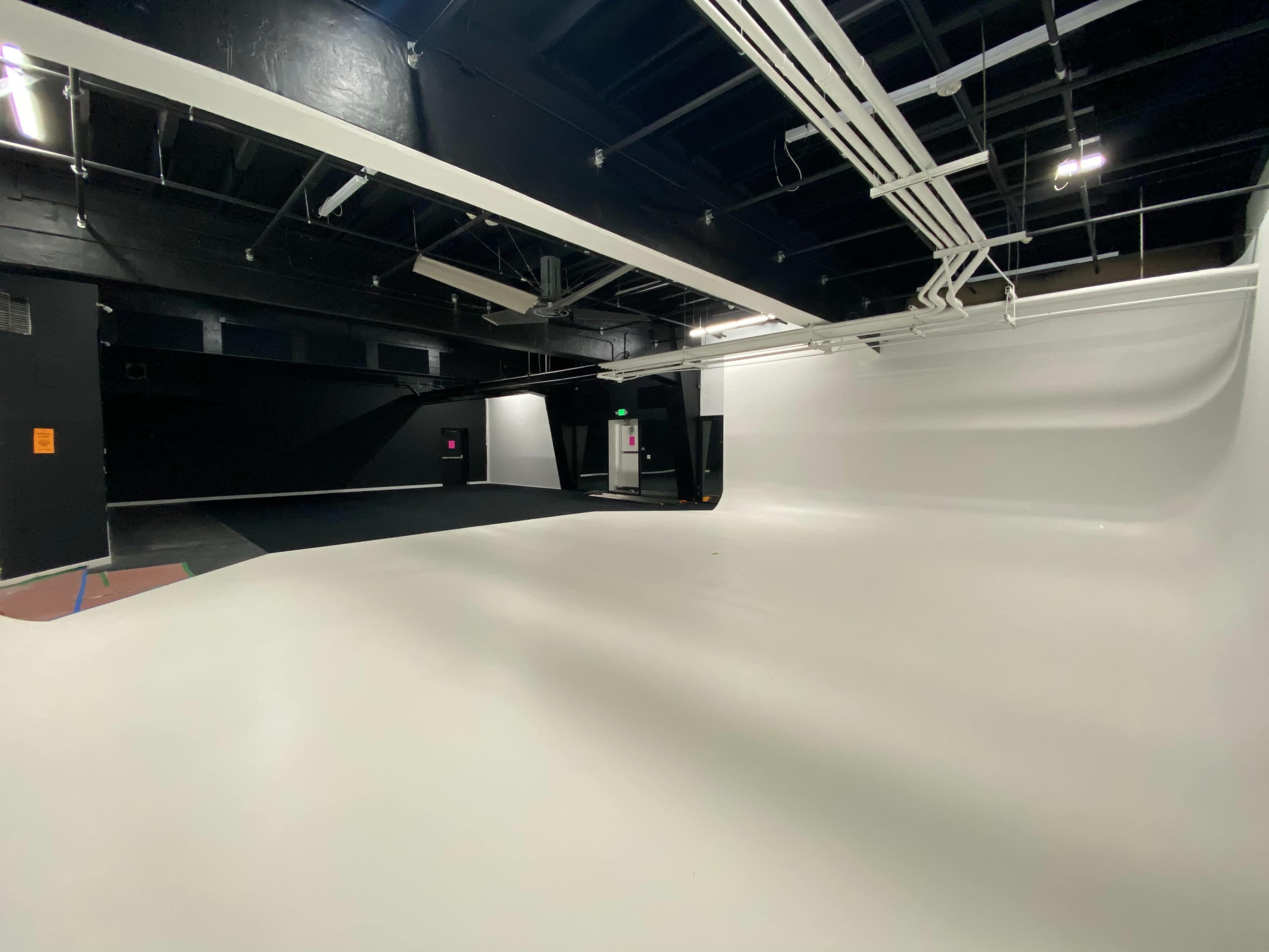 A spacious studio with smooth white walls and a curved backdrop, equipped with overhead lighting and various cables.