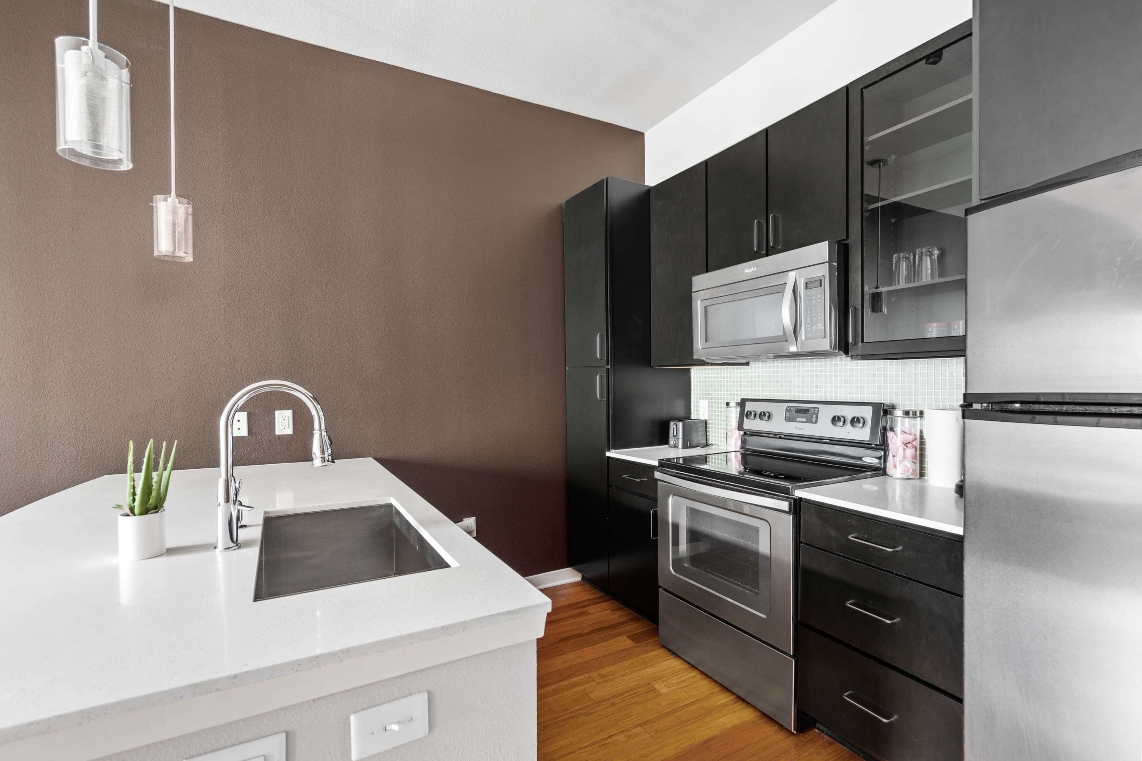 A modern kitchen features black cabinetry, stainless steel appliances, and a white countertop with a sink.