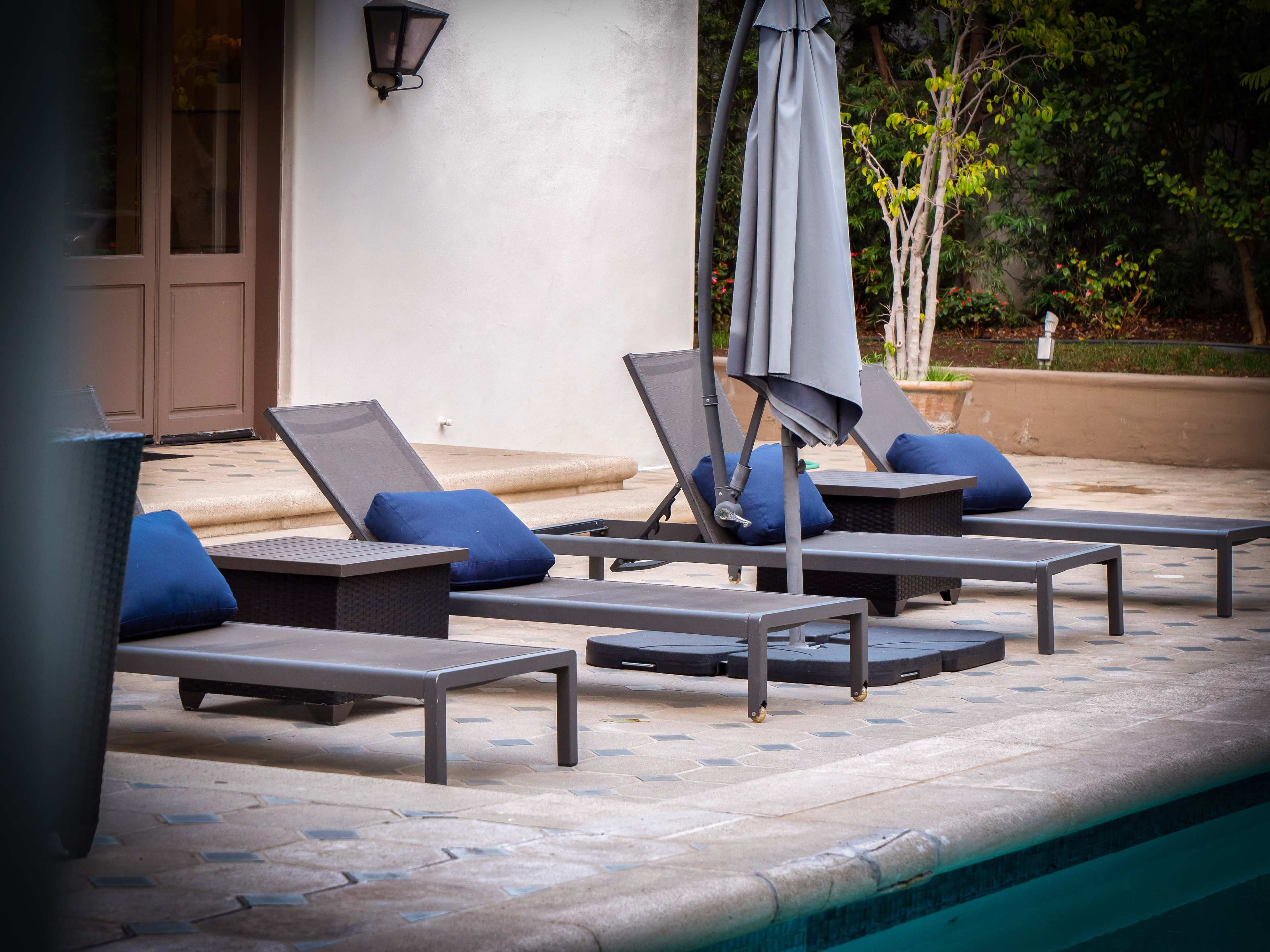 Several lounge chairs with blue cushions arranged by a swimming pool area, accompanied by a gray umbrella.
