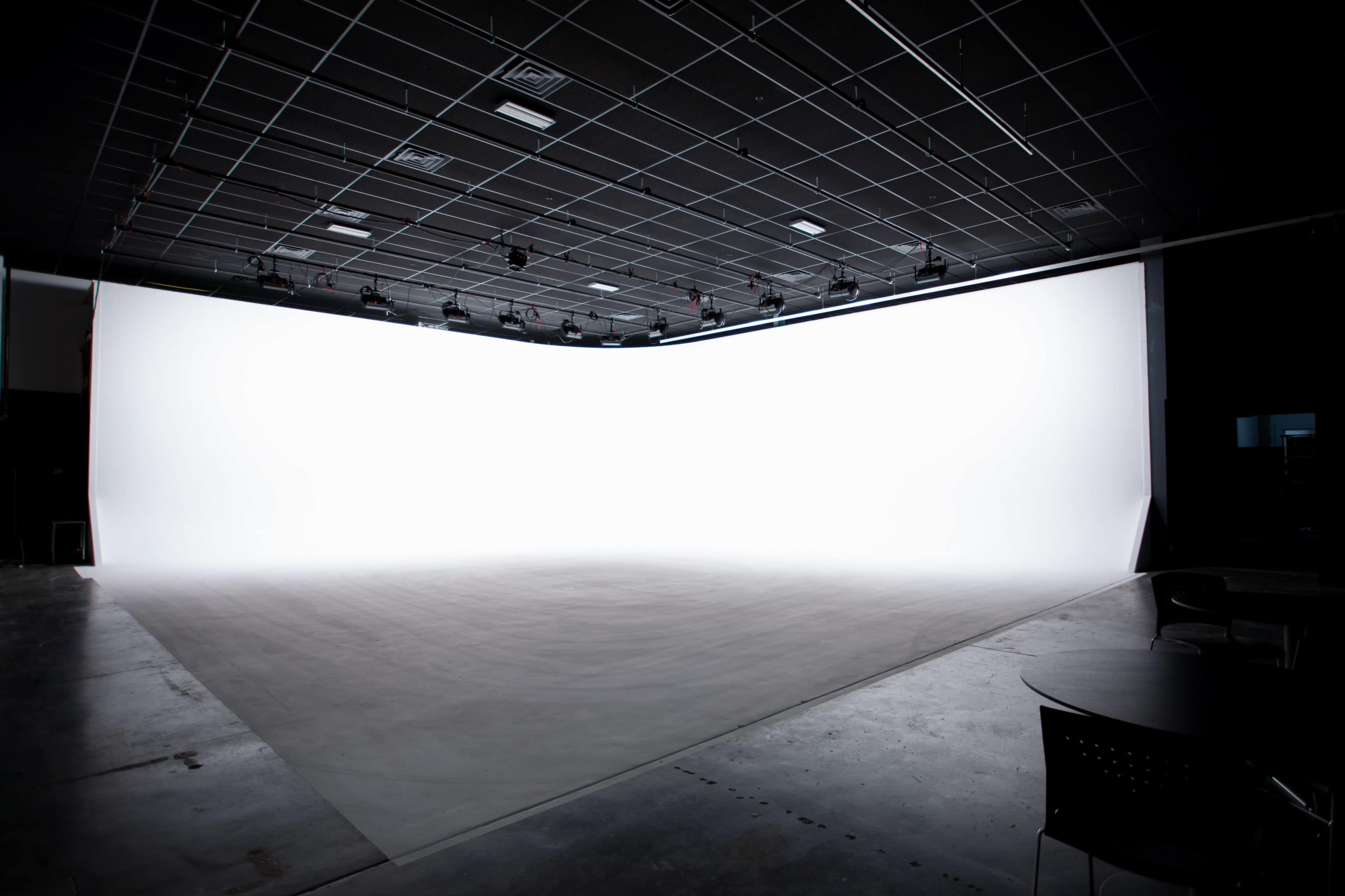 A spacious studio features a large white backdrop with a smooth floor and overhead lighting.