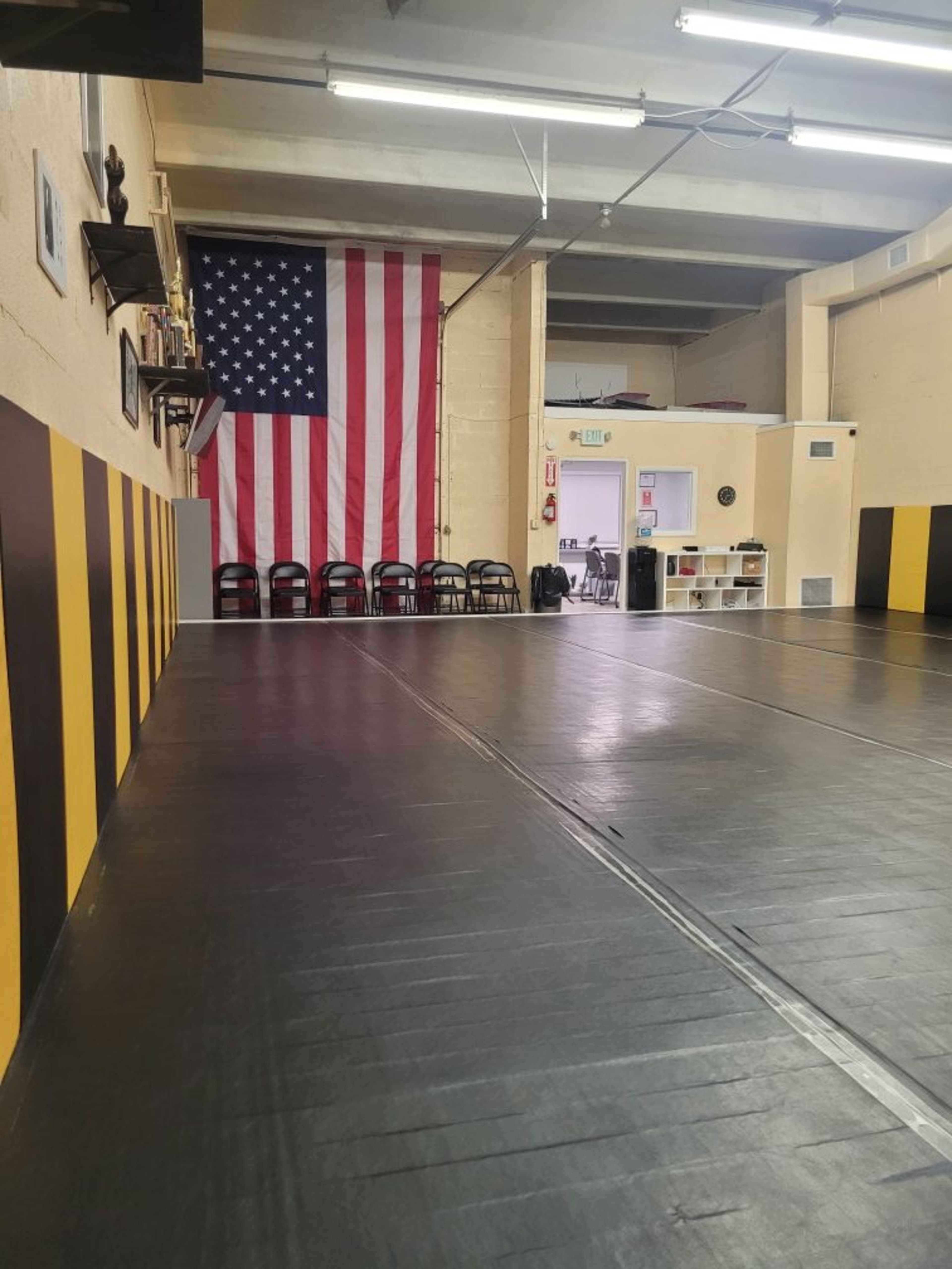 The image shows a spacious indoor training area with a large American flag hanging on the wall and a row of black chairs against the opposite wall.