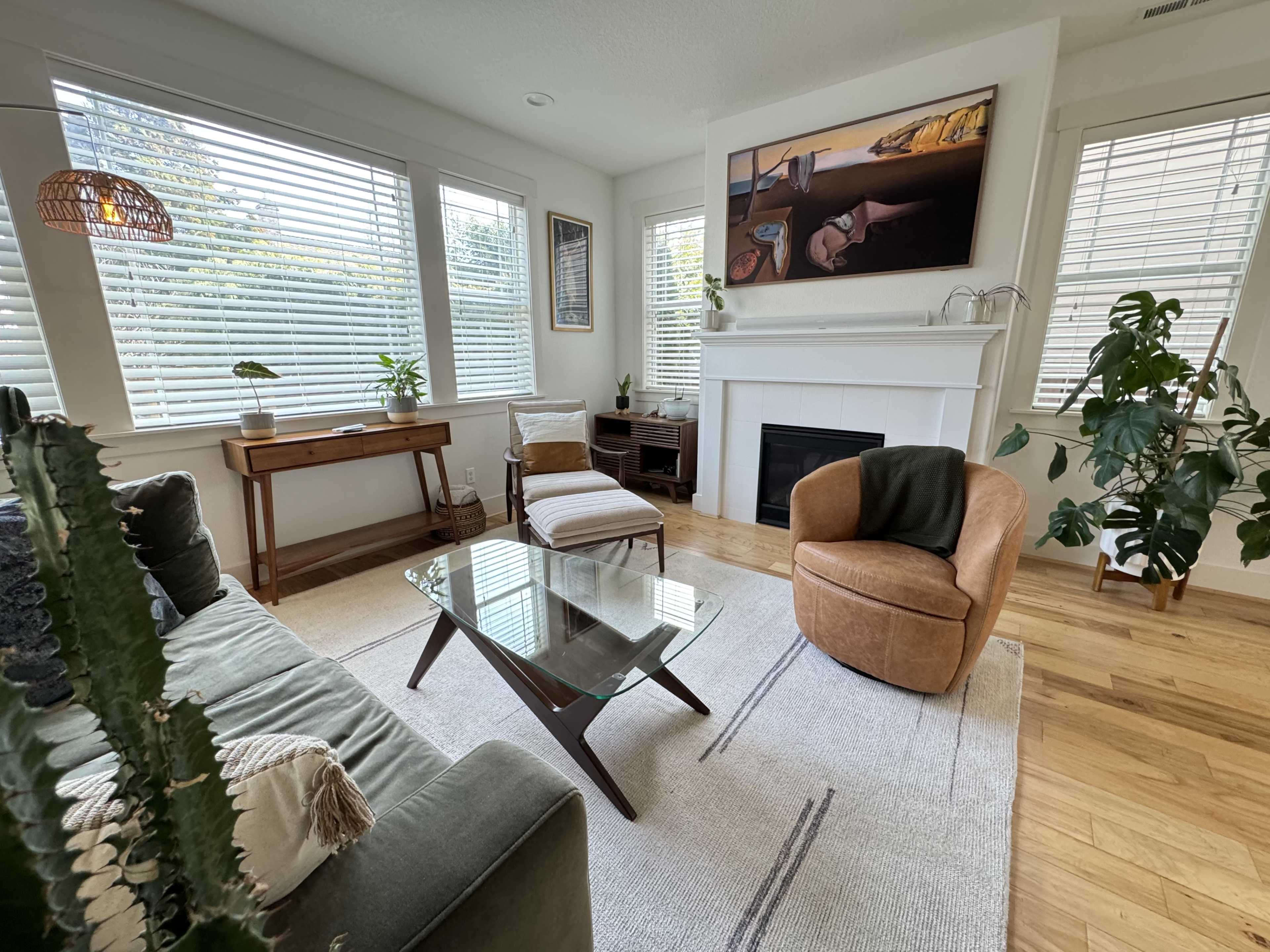 A cozy living room features a green sofa, an armchair, and a glass coffee table, with large windows allowing natural light to fill the space.