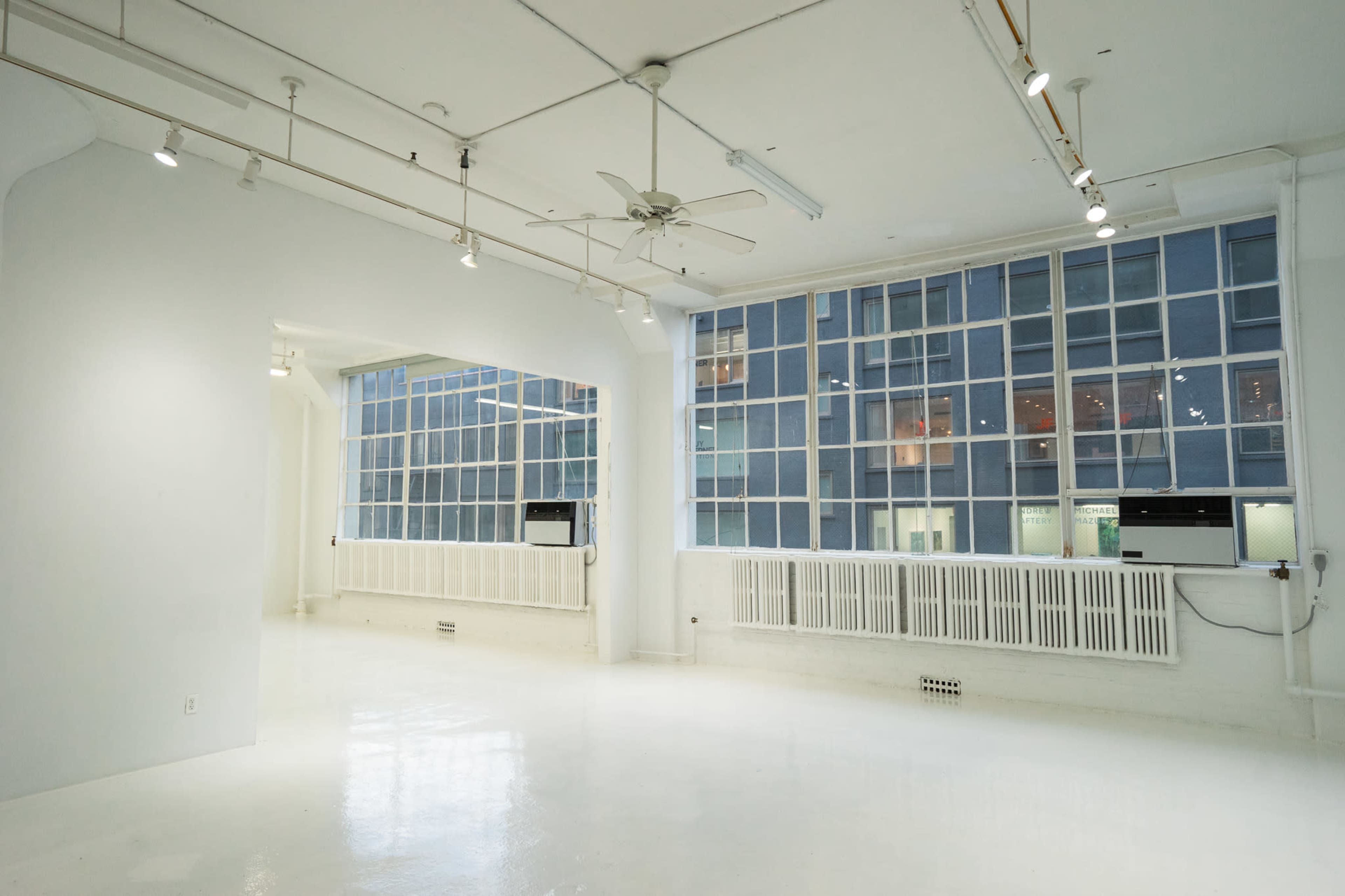 A spacious, brightly lit room with white walls and large windows showing a cityscape outside.