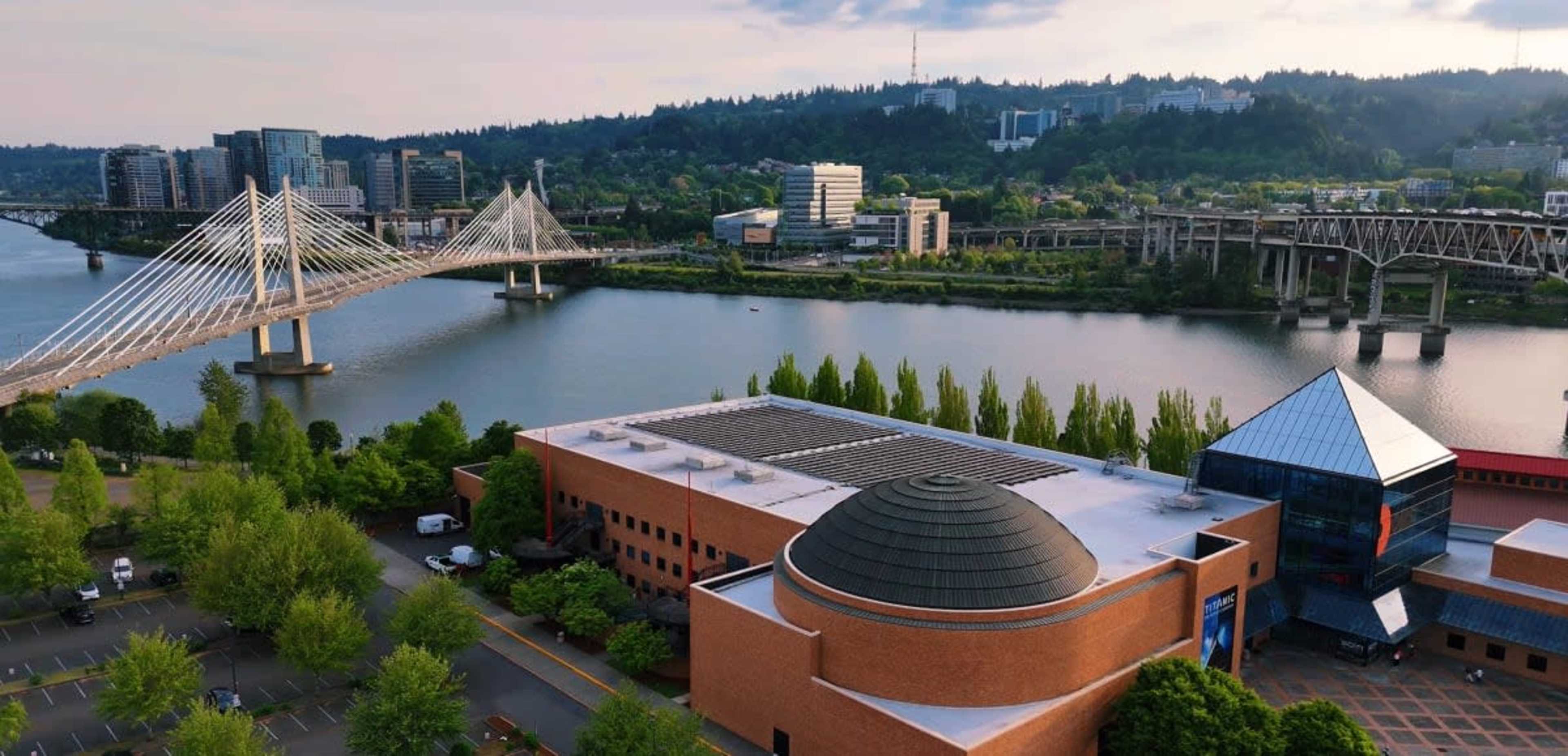 The image shows a riverfront view of a city, featuring a bridge, modern buildings on the opposite bank, and a dome-topped structure in the foreground.