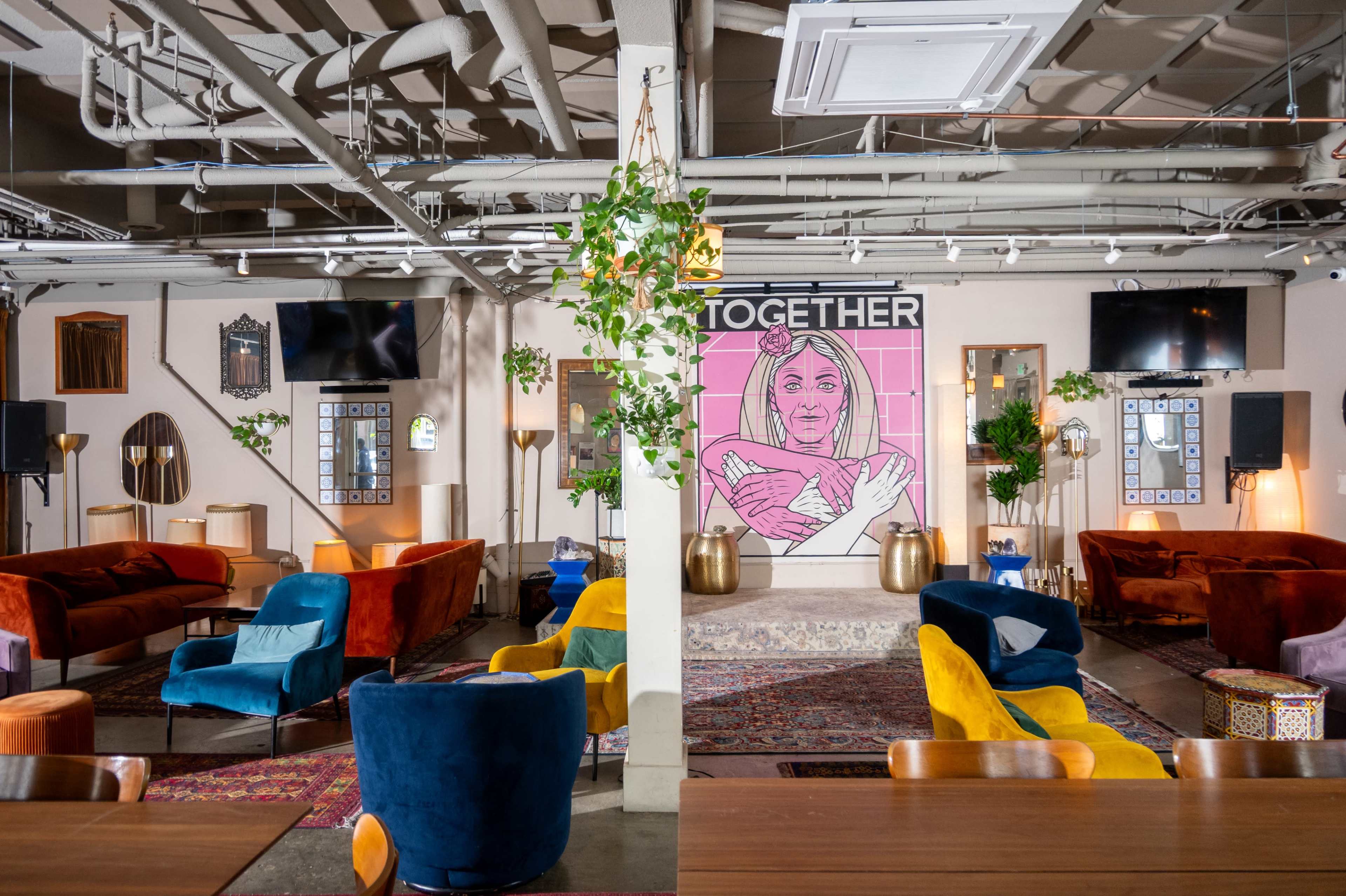 The image shows a spacious lounge area with colorful seating, decorative plants, and a large mural featuring a woman's face labeled "TOGETHER" on the wall.