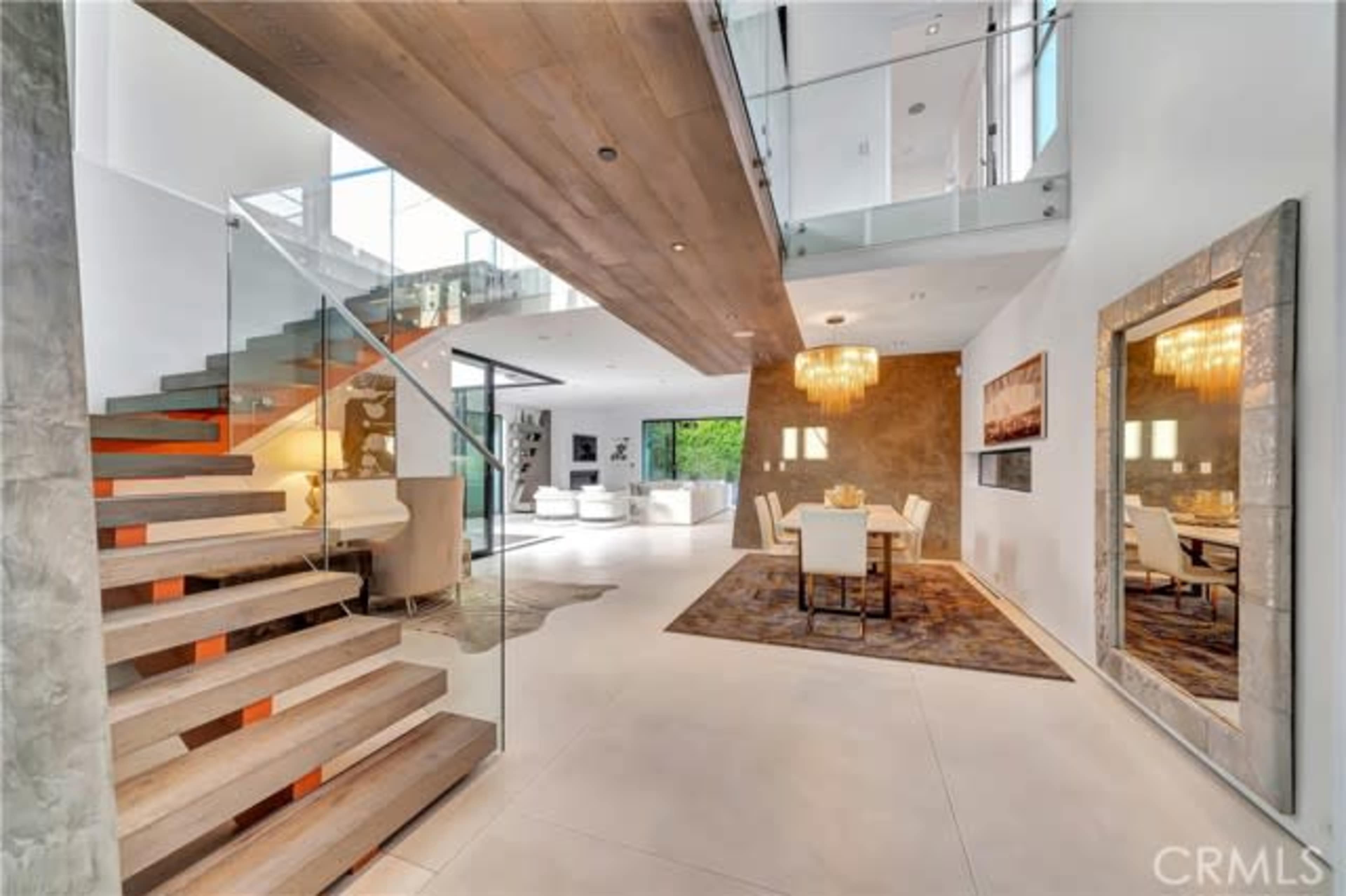 The image showcases a modern open-concept living space with a staircase, dining area, and large windows allowing natural light.